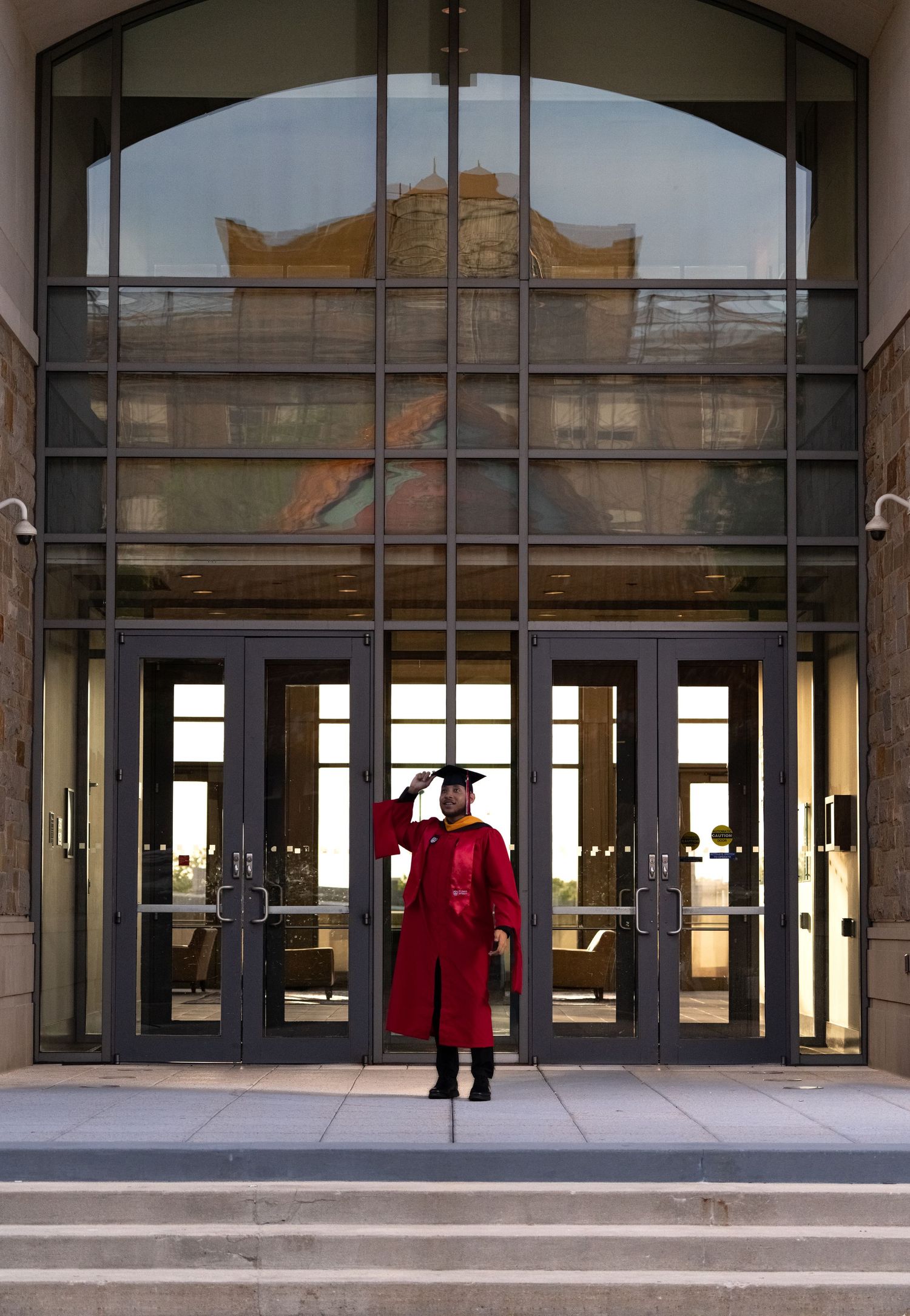 Modern glass building entrance with red graduation attire visible through reflective windows.