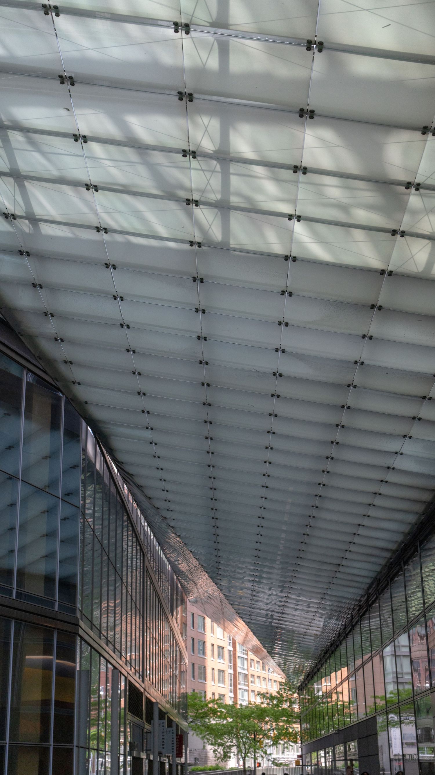 Modern architectural walkway with glass ceiling and geometric patterns casting shadows.