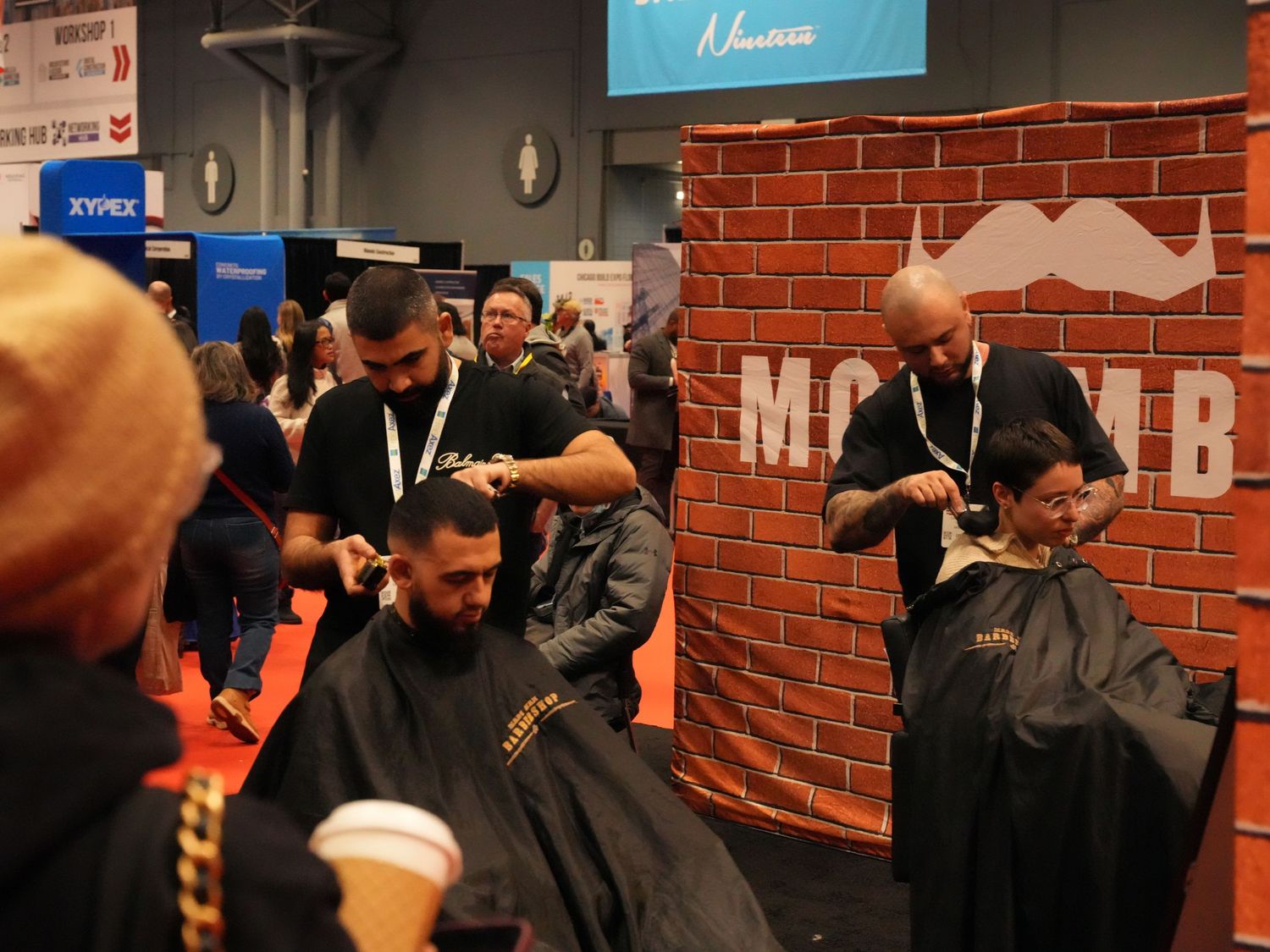 Barbers cutting hair at a Movember charity event booth inside a convention center.
