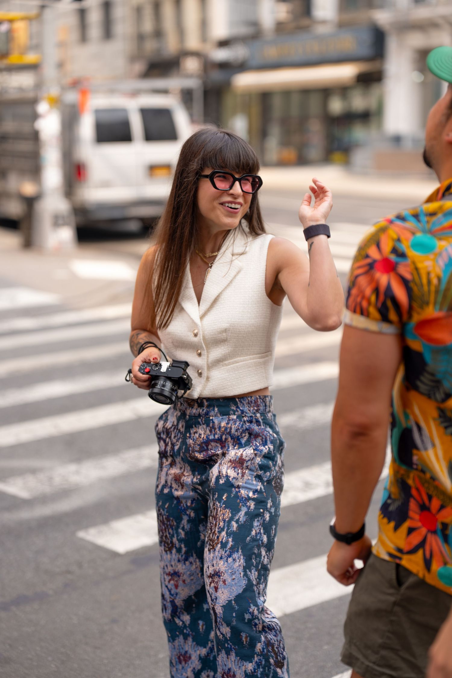 Person wearing white top and patterned blue pants walking on crosswalk in urban setting.