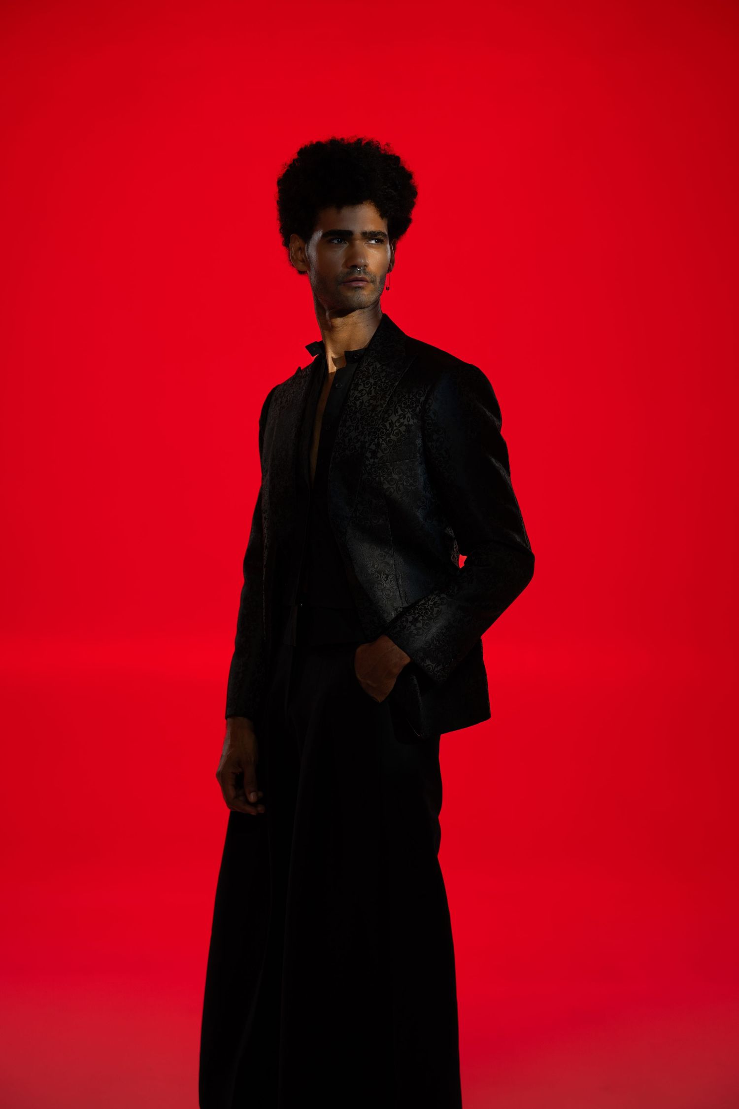 Moody fashion photography with dark clothing contrasting against bright red background.