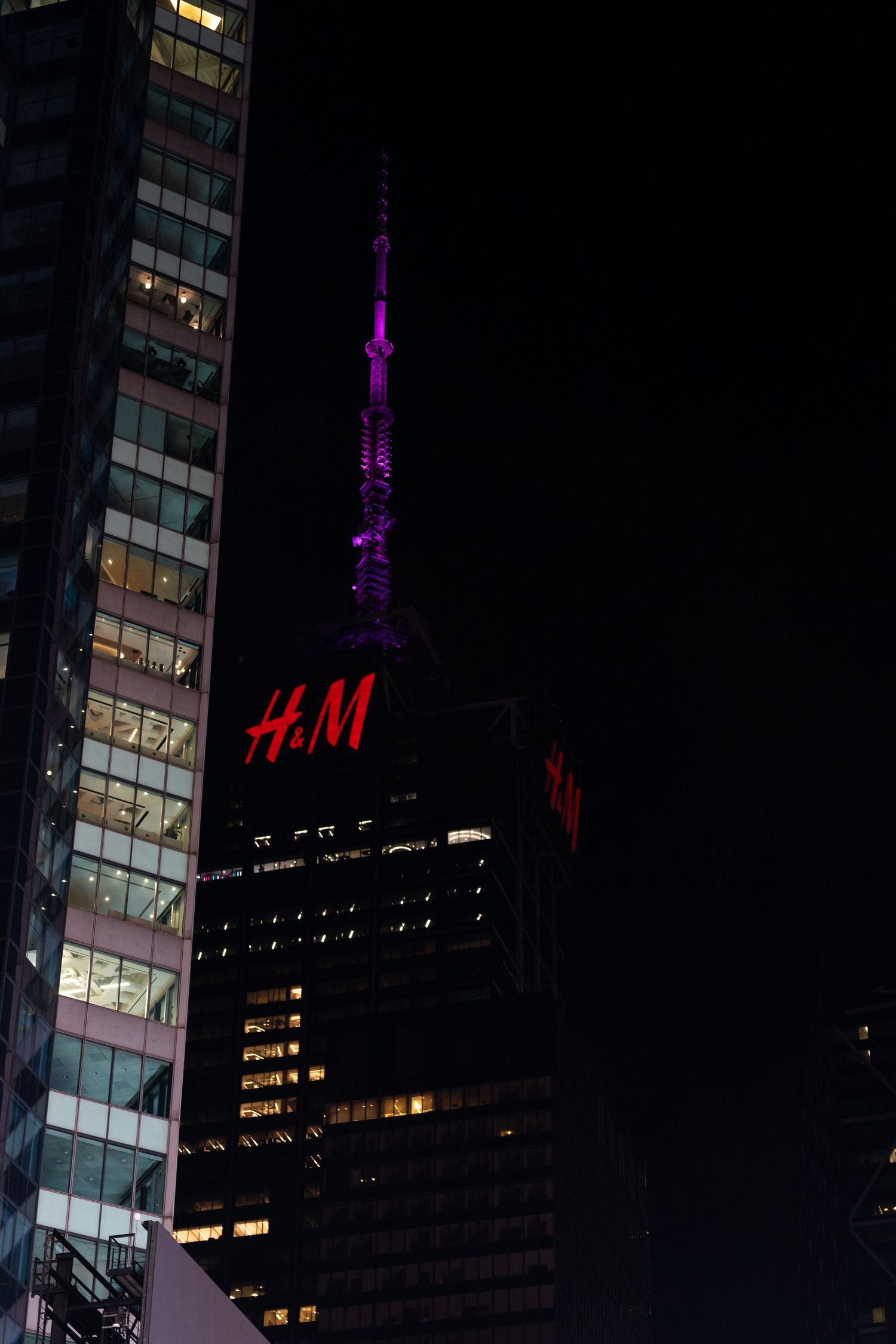 H&M store sign glows against dark city skyline with purple-lit tower in background.