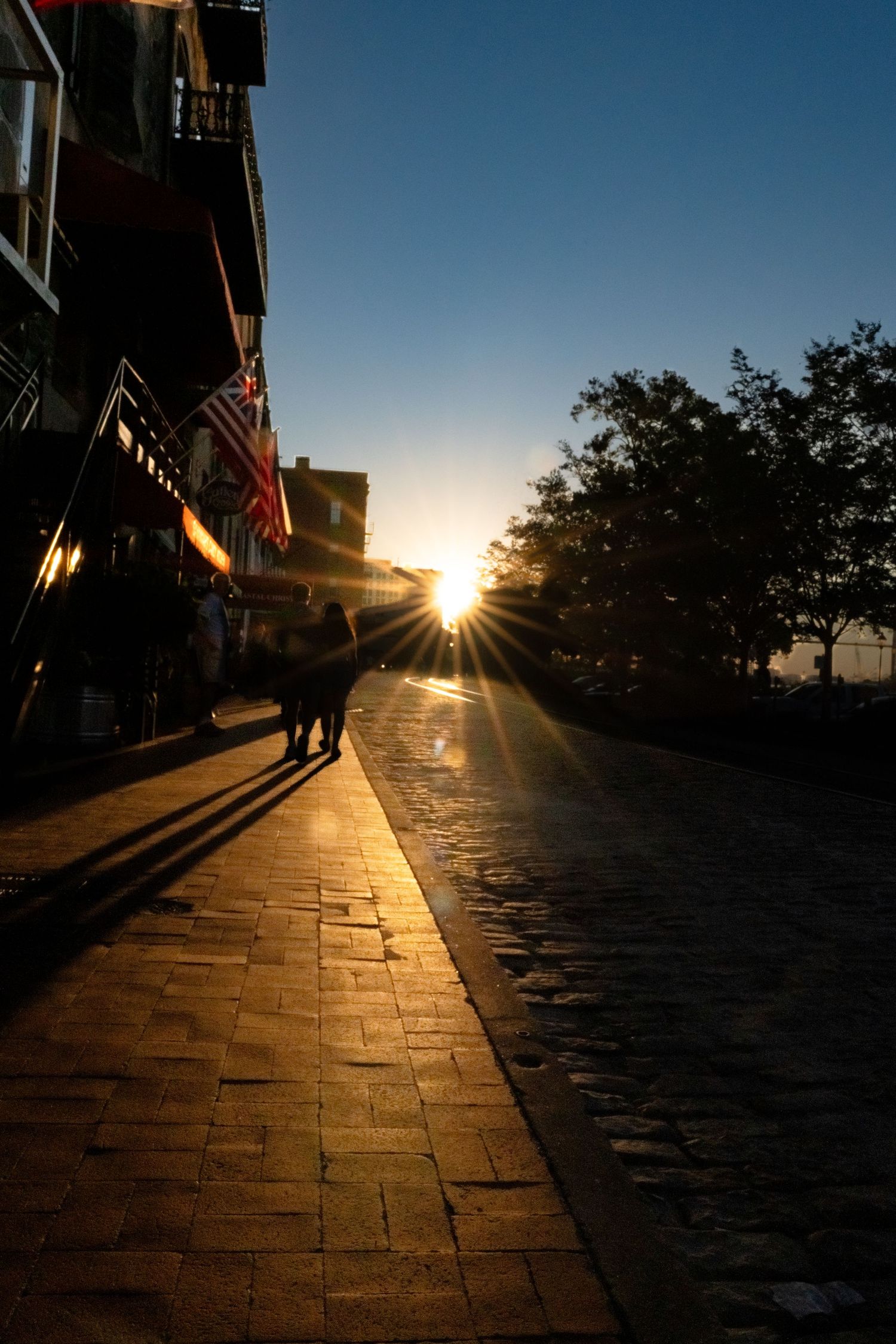 Cobblestone street at sunset with dramatic shadows and sunburst through buildings.
