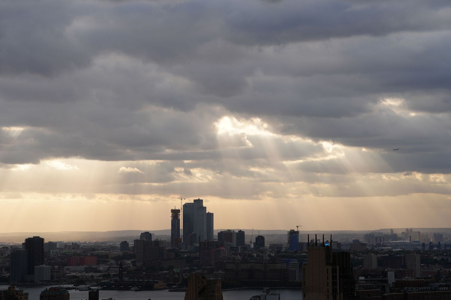 Dramatic cityscape silhouette with sunbeams breaking through storm clouds at sunset.