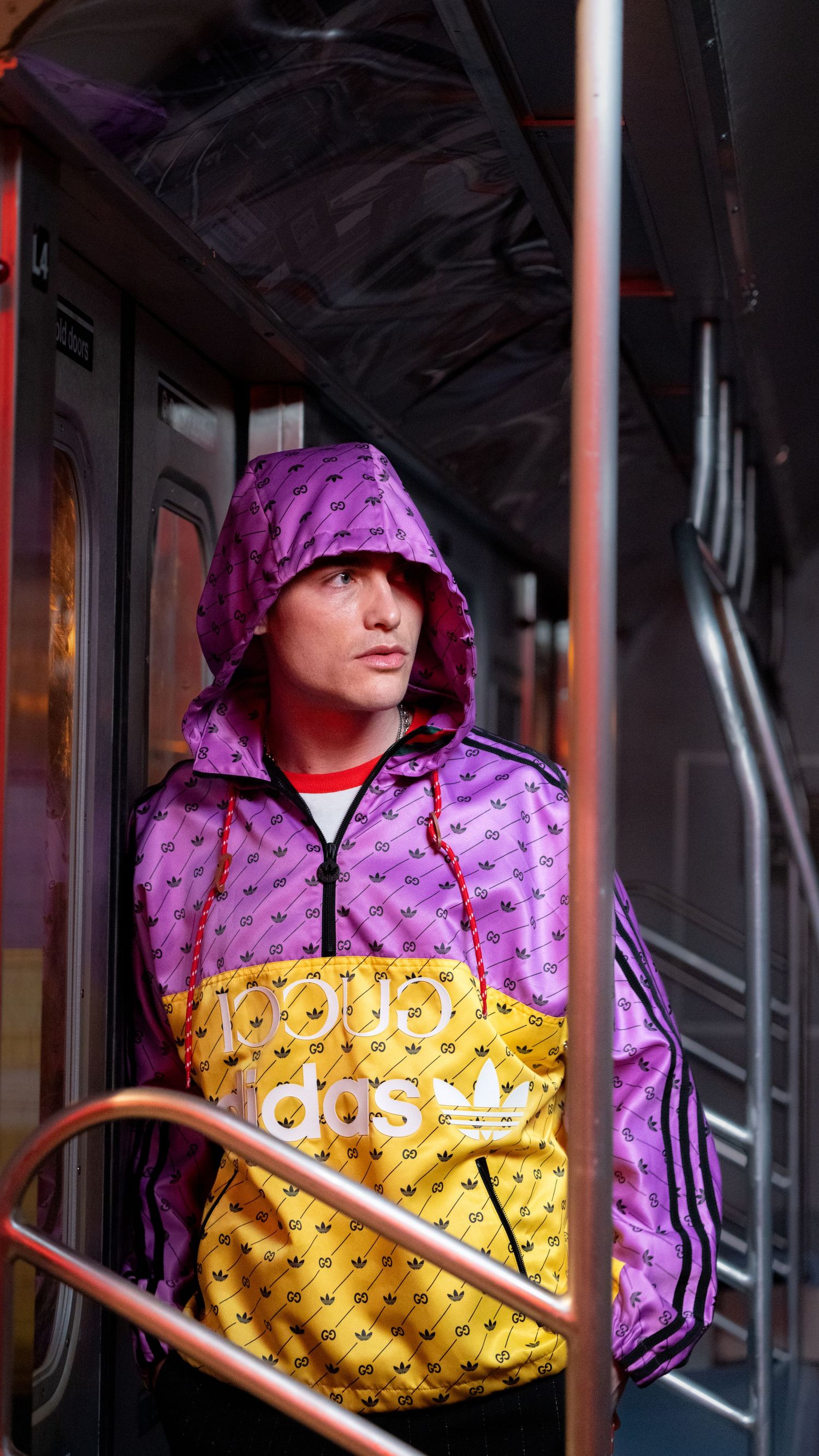 Person wearing purple and yellow Adidas hoodie posing in dimly lit subway car.