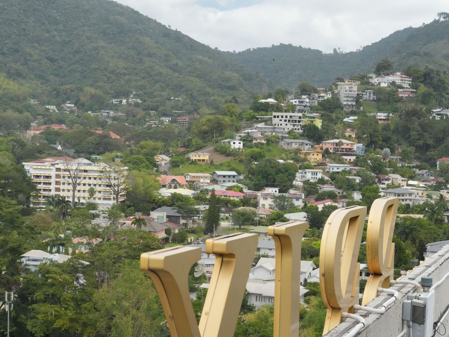 Panoramic mountain view of a residential hillside neighborhood with houses nestled among lush green trees.