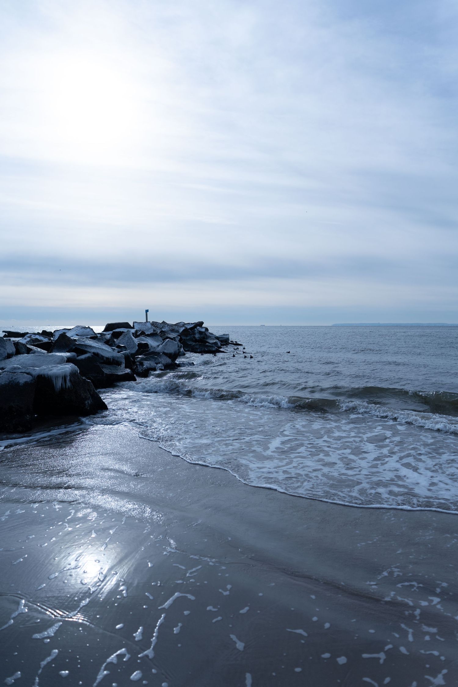 Winter seascape with rocky jetty and gray waves under overcast sky.