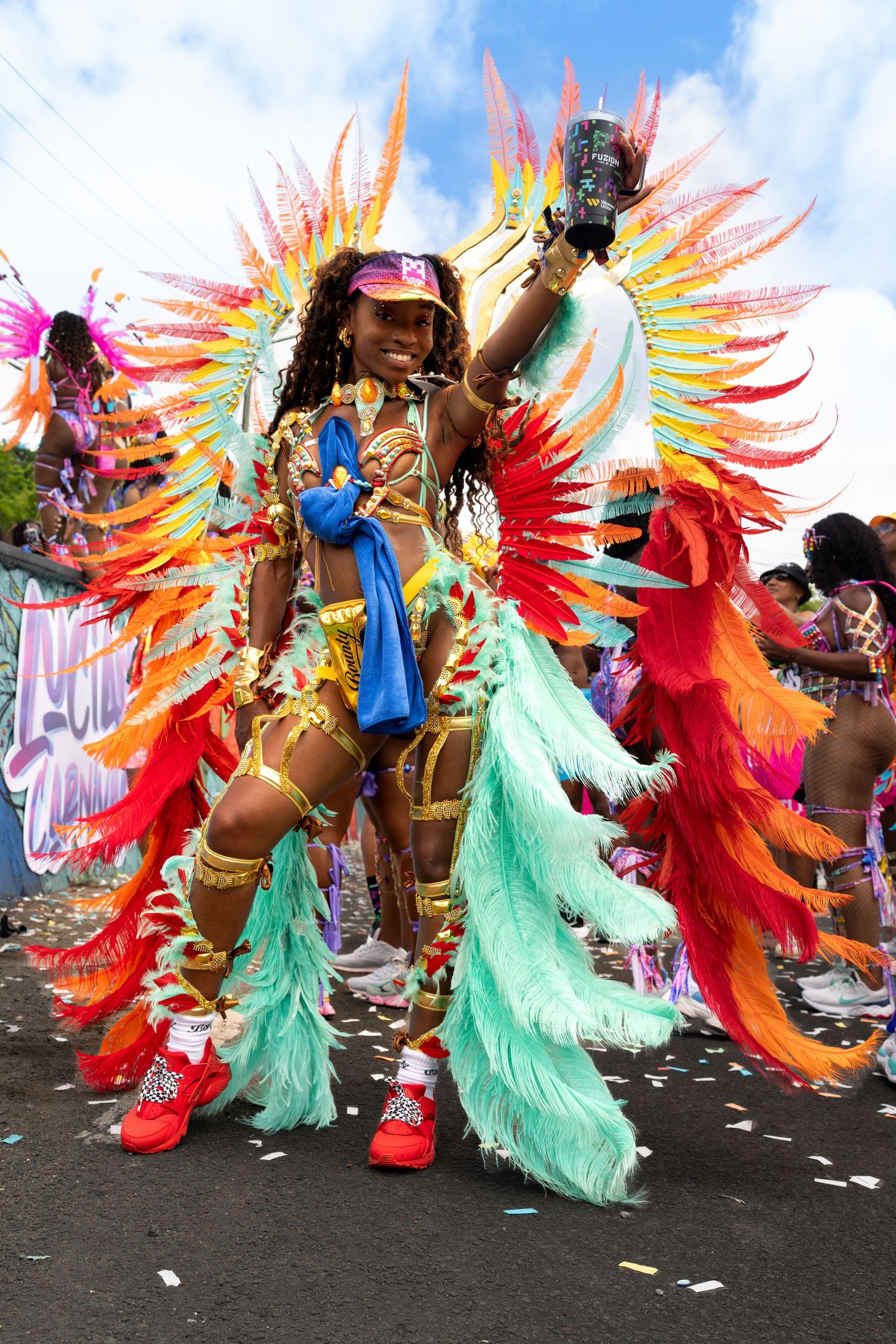 Dancers in bright feathered costumes featuring turquoise, red, and orange plumes perform in a carnival parade.