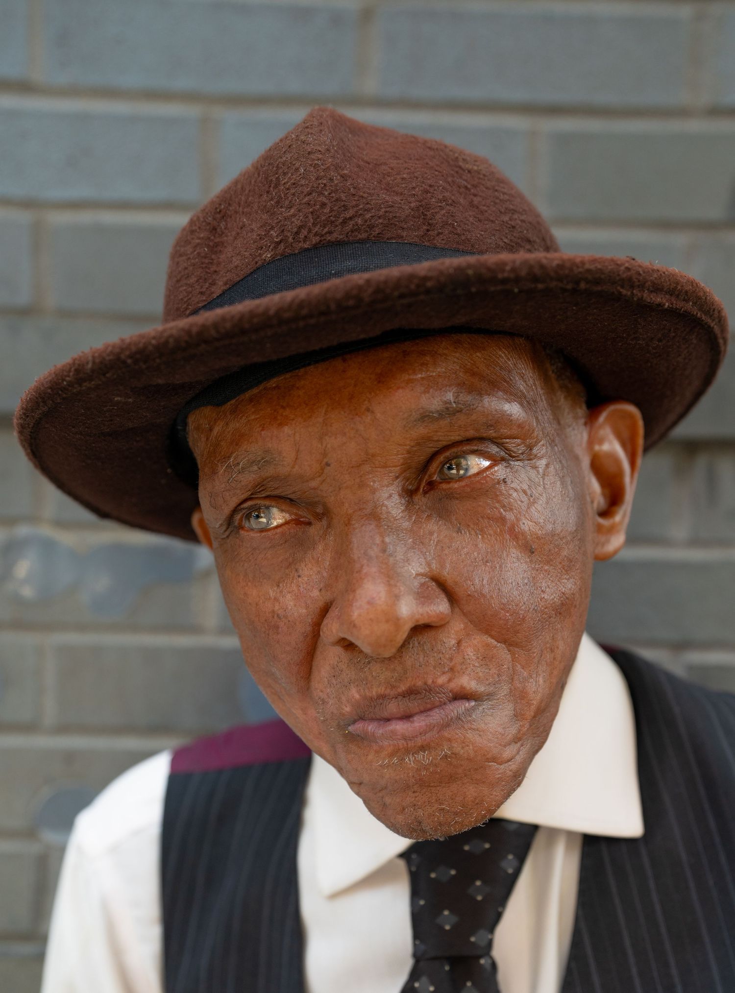 A person in a brown hat and formal attire shown in multiple close-up shots.
