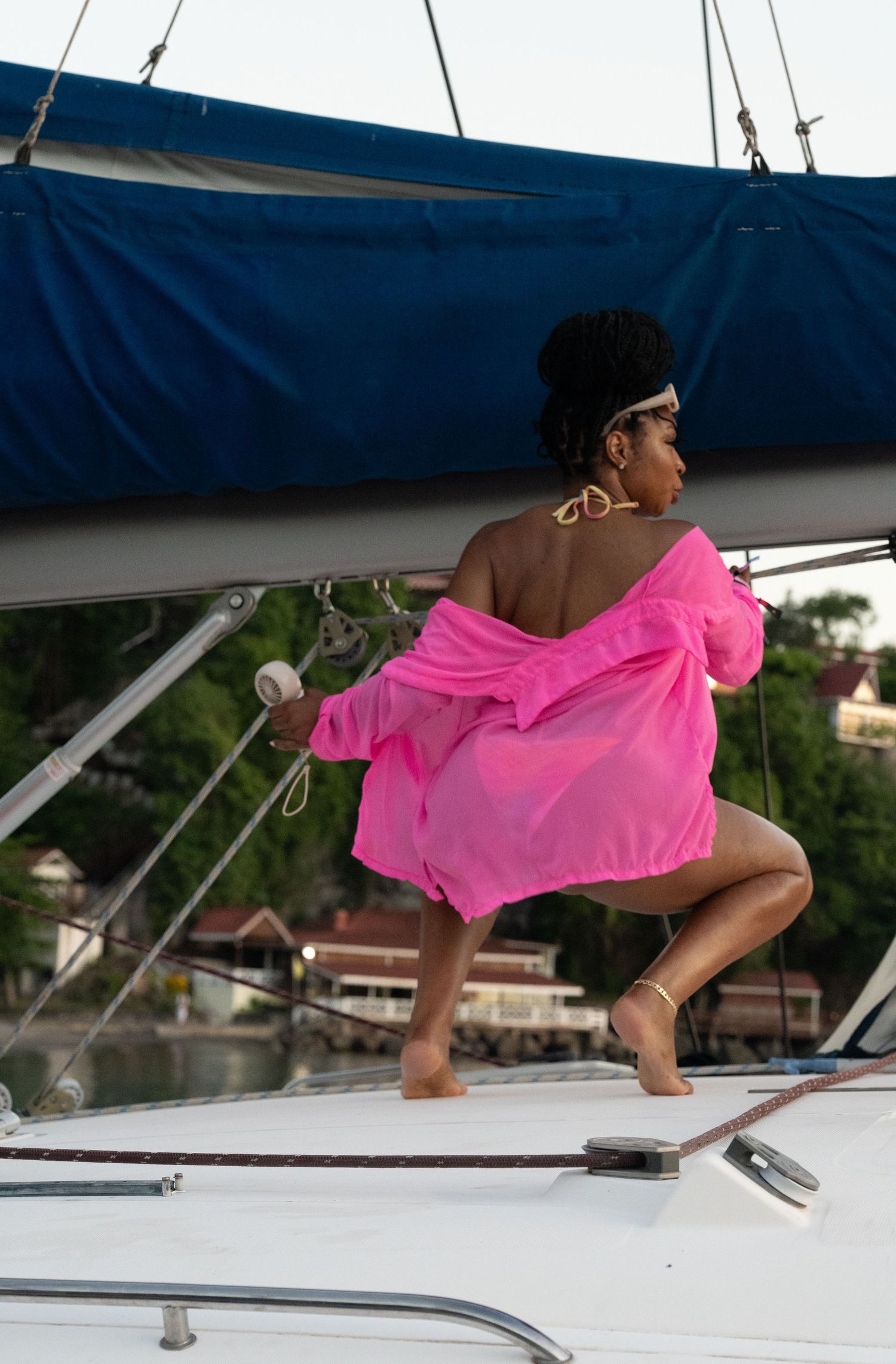 Person in flowing pink dress dancing on white boat deck at sunset.