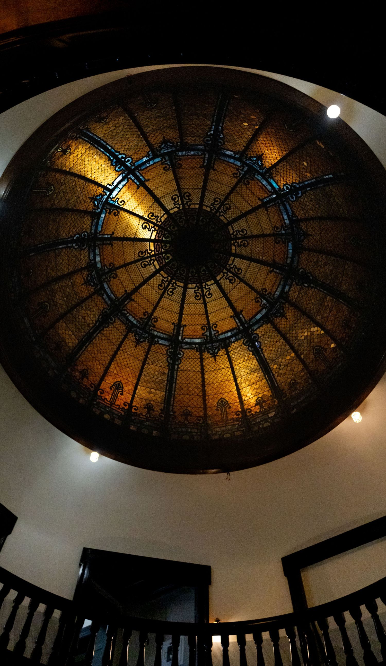 Ornate stained glass dome ceiling with amber lighting and geometric metal framework creates dramatic architectural focal point.