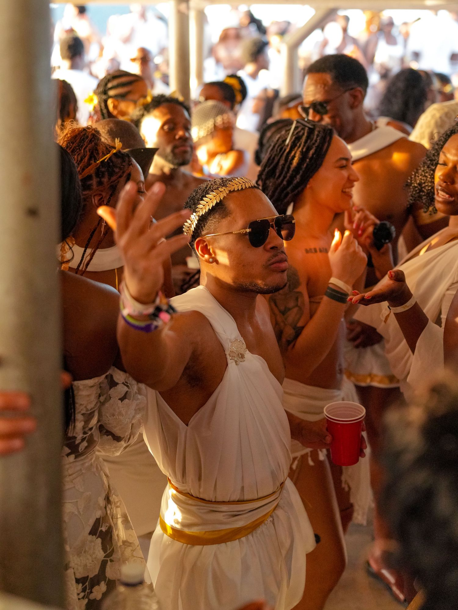 A group of people in white togas and gold accessories dancing and celebrating at what appears to be a Roman-themed party.