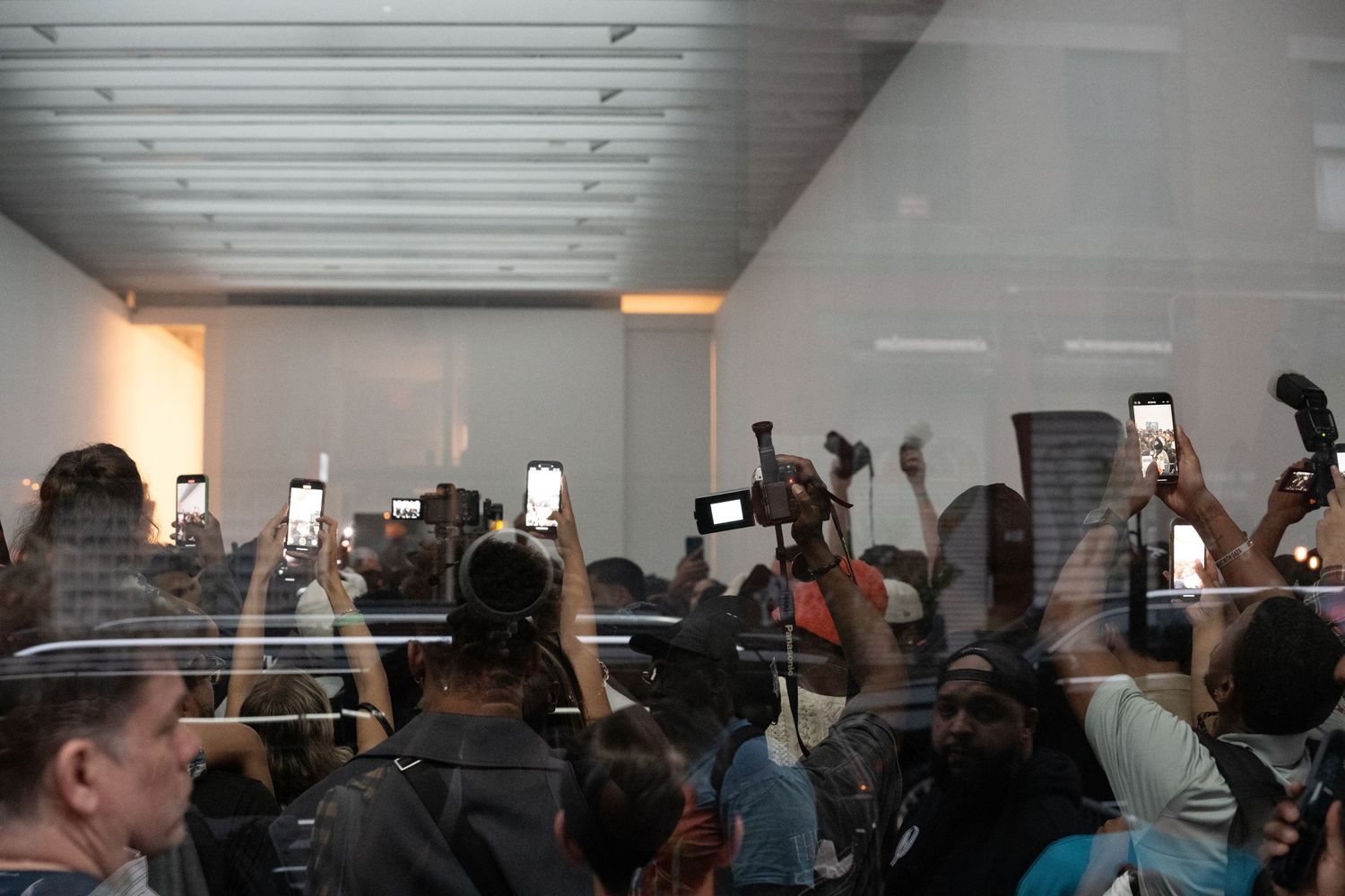 Crowd holding up phones in a brightly lit indoor space with white ceiling.