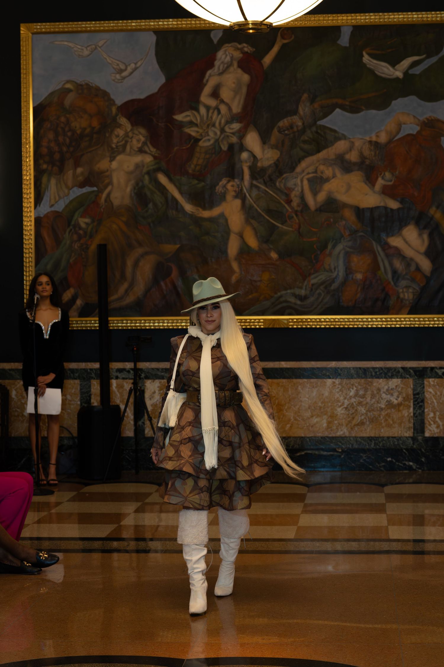 Dancers in white and black outfits perform on a polished floor beneath decorative wall murals.