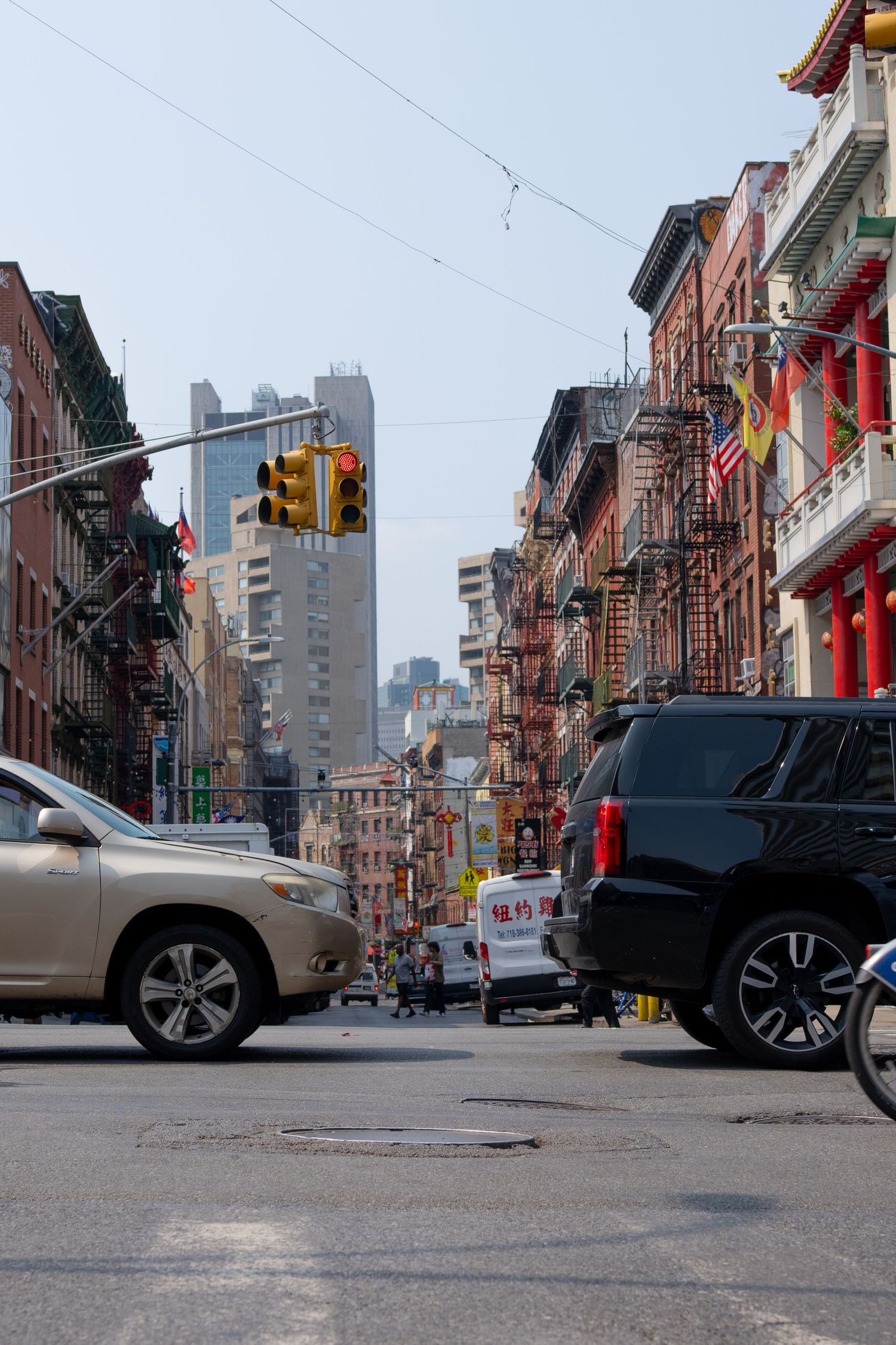 Urban street scene in New York's Chinatown with historic buildings, parked cars, and fire escapes.