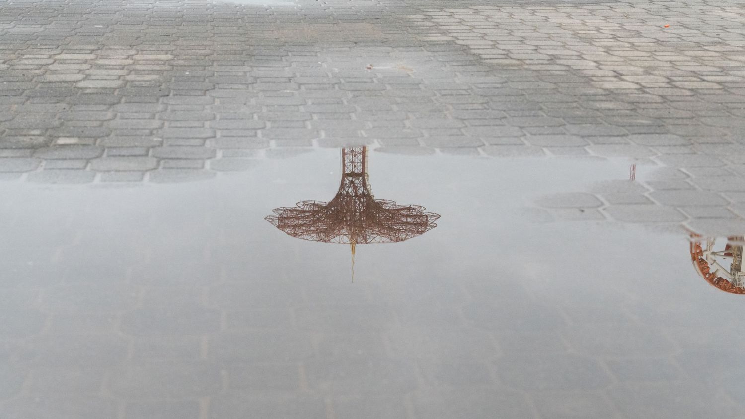 Wet cobblestone pavement reflecting amusement park structures.