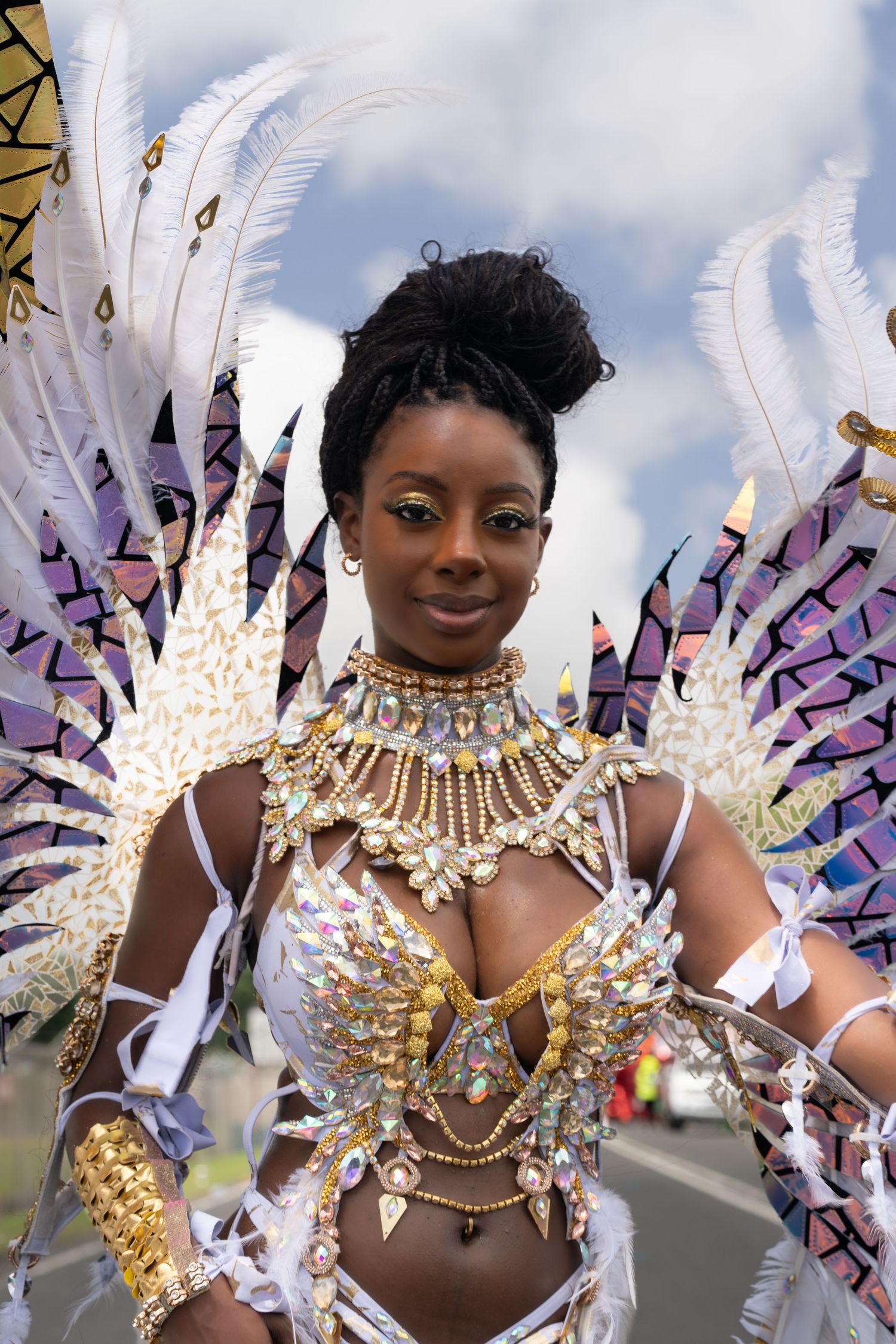 Carnival performer wearing elaborate white and gold feathered costume with purple accents.