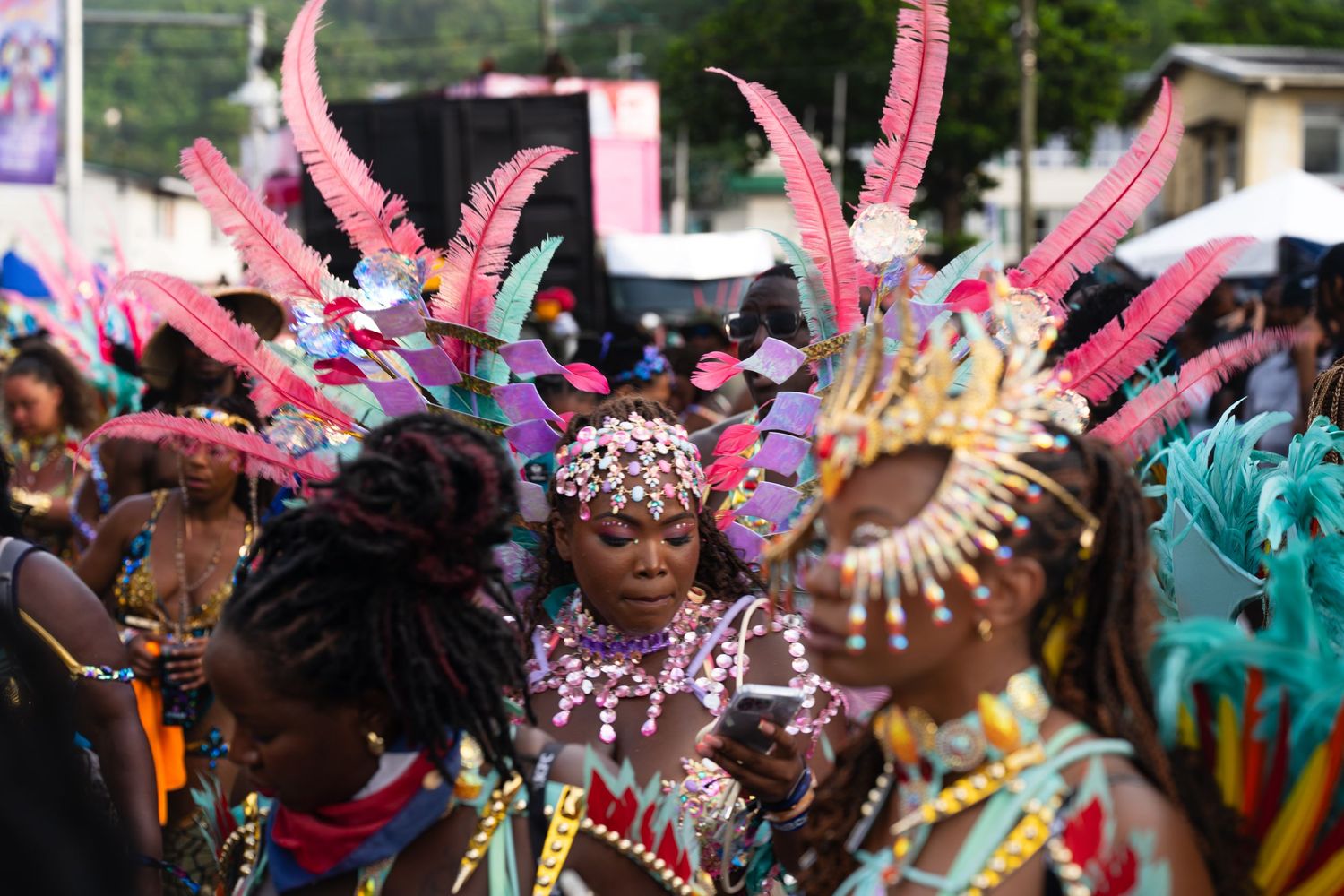 Colorful carnival dancers wearing vibrant pink feathered headdresses perform during a festive parade celebration.