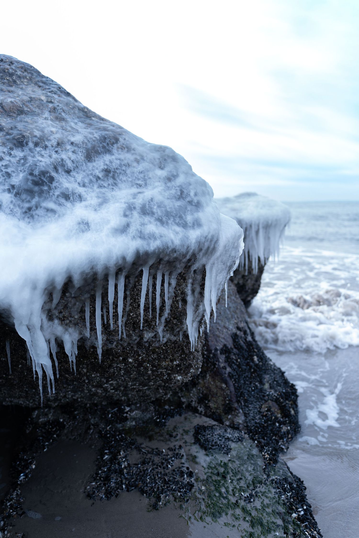Dramatic icicles hanging from dark rocky cliff face above ocean waves.
