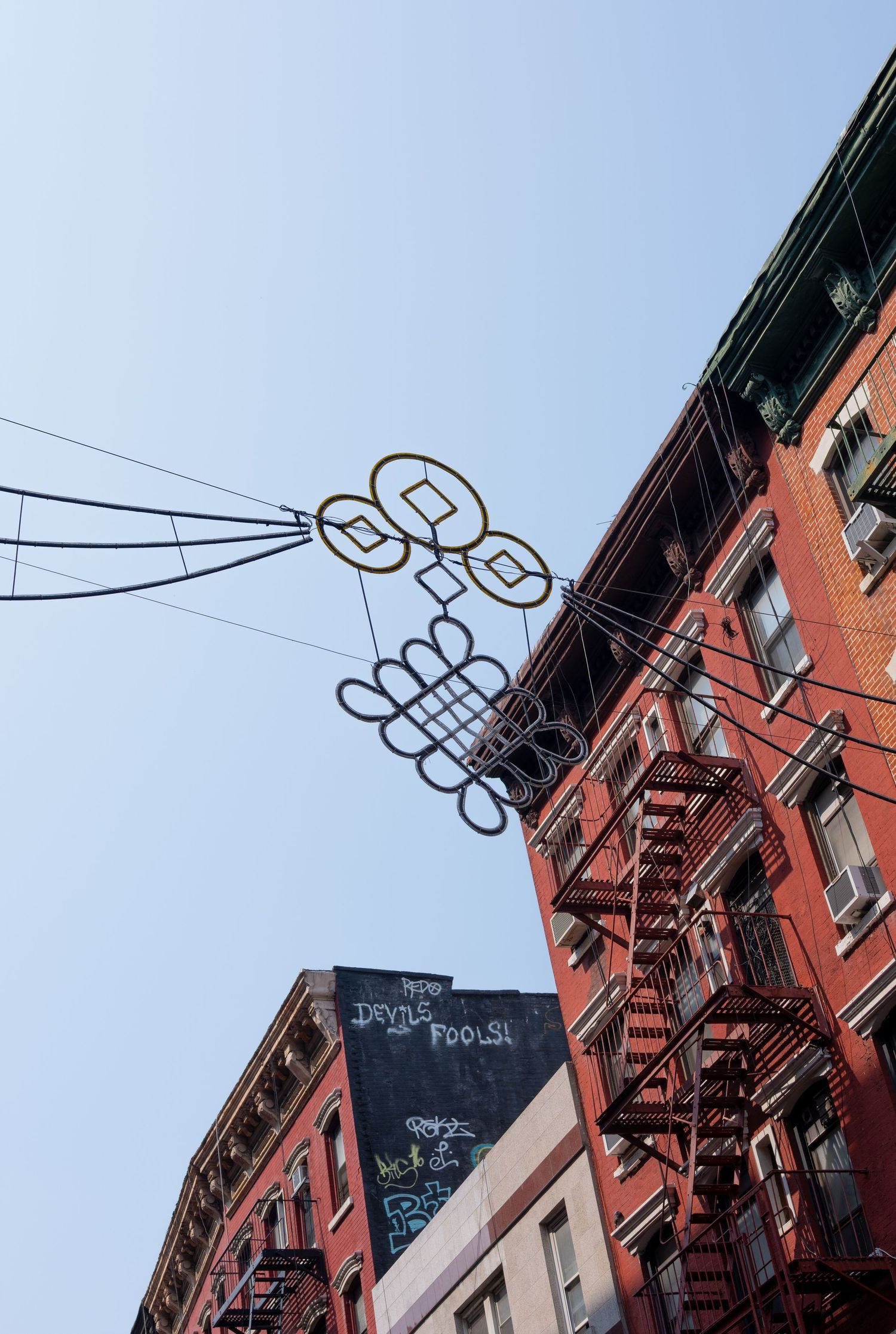 Looking up at red brick buildings with fire escapes against blue sky.