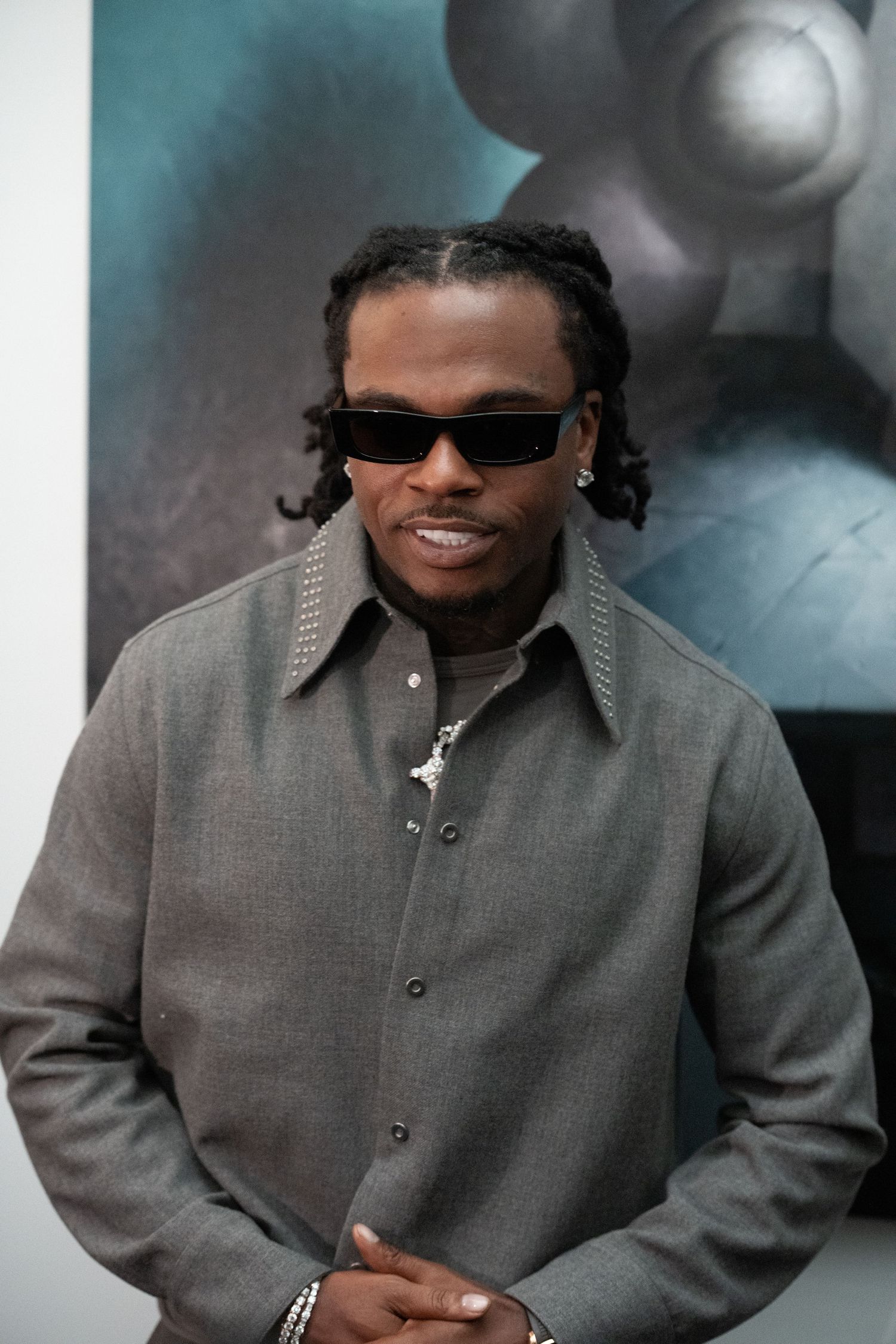 Person wearing a gray button-up jacket and sunglasses against a teal background.