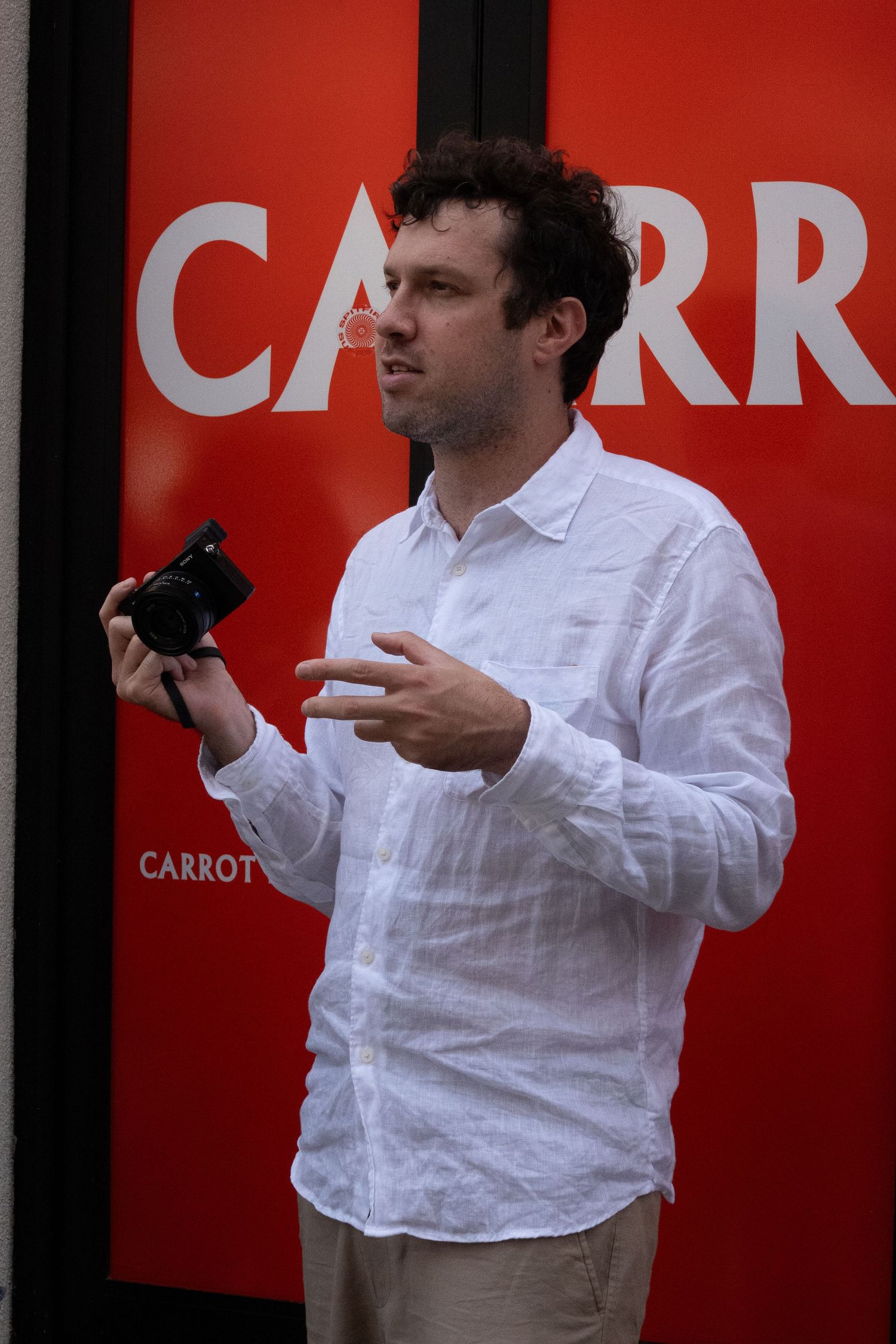 Person in white shirt photographing against red wall with 'CARROT' text.
