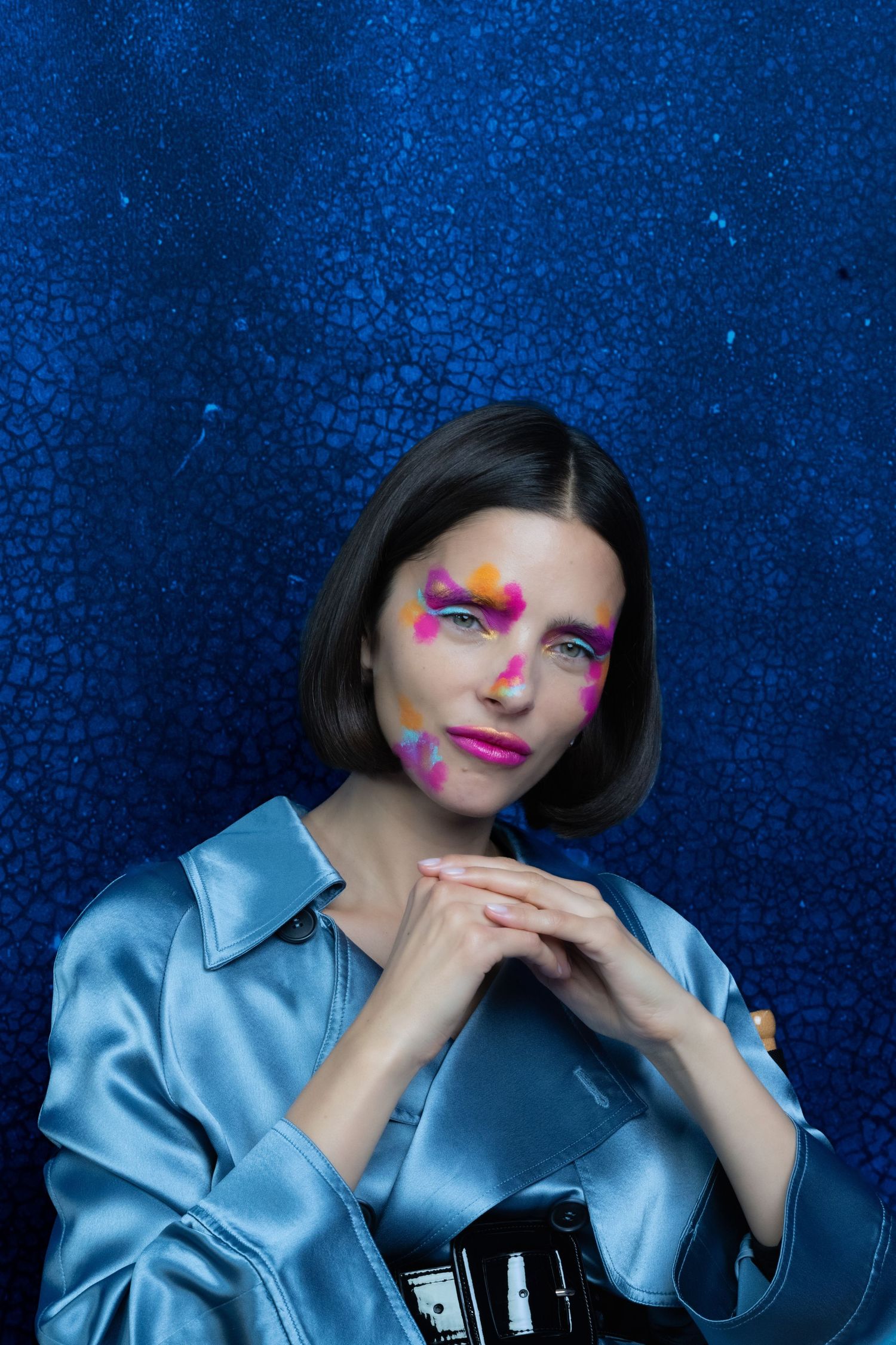 Fashion portrait against blue background featuring bright pink eye makeup and a light blue silk blouse.