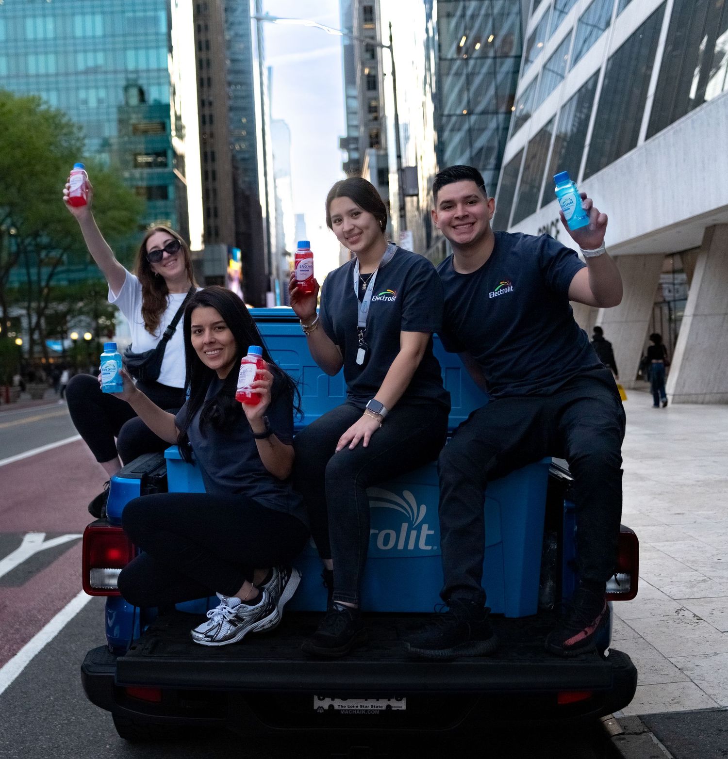 Group sitting and posing playfully on a blue branded vehicle outside an office building.