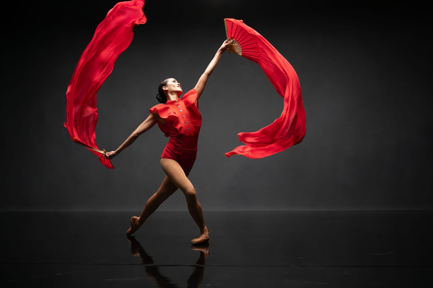 Dancer in red flowing fabric performs dramatic movements against dark background.