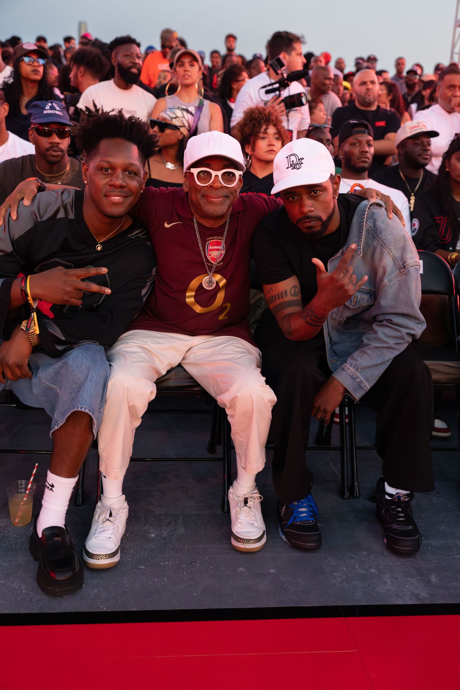 Group of friends sitting together at an outdoor event wearing casual streetwear.