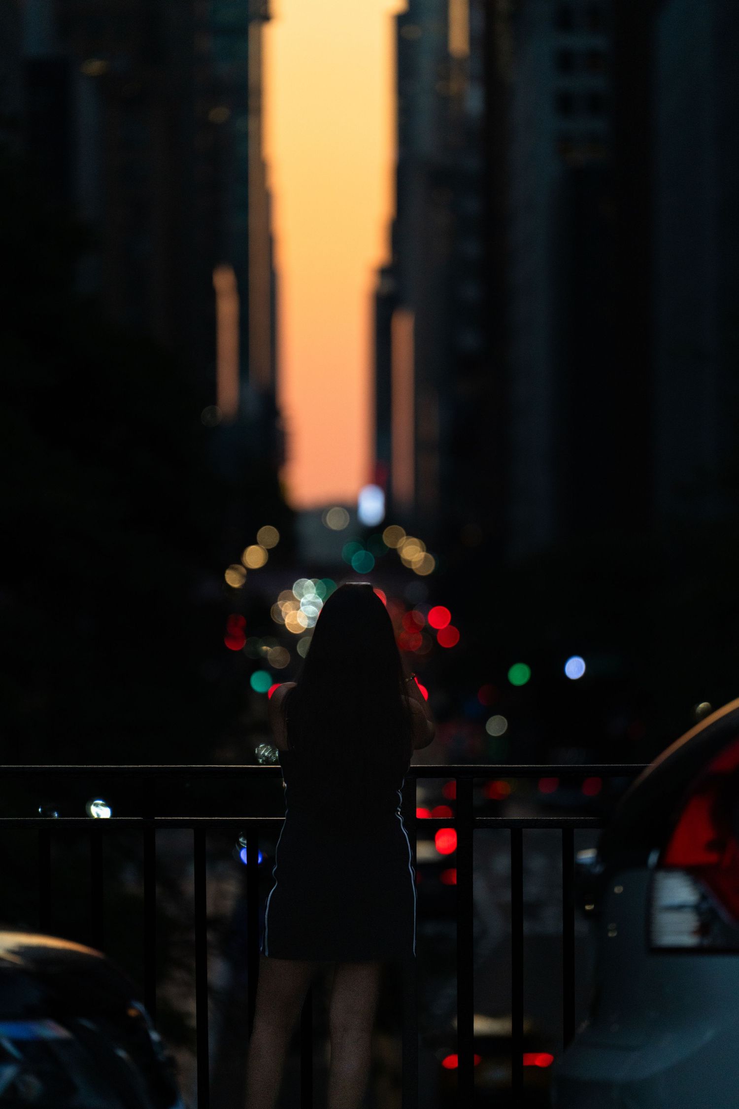 Silhouettes of people and cars against warm sunset light in an urban setting.