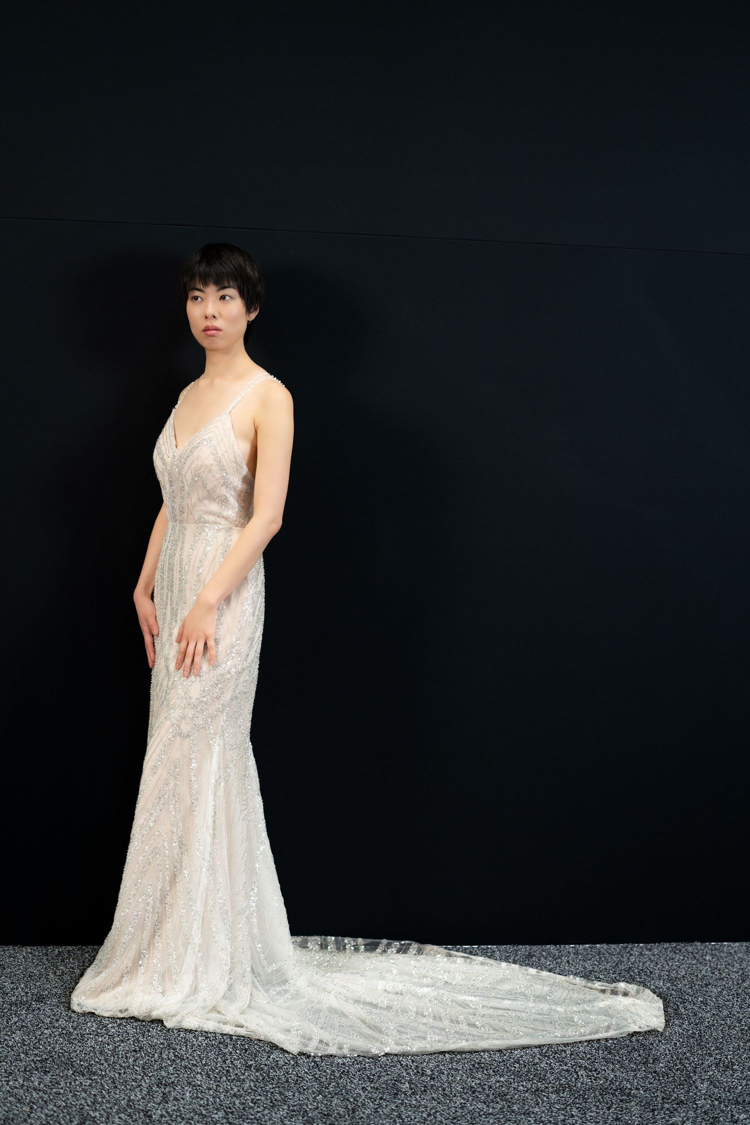 Long white sequined dress with train photographed against dark background.