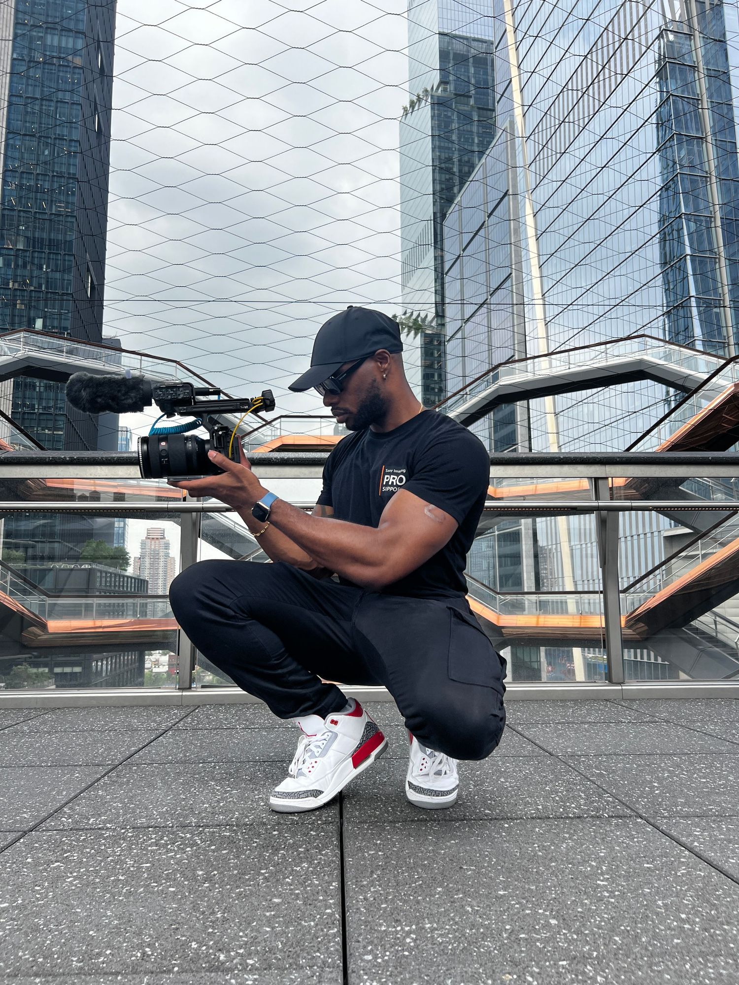 Cinematographer crounching on ground taking creative angle shots near modern glass buildings.