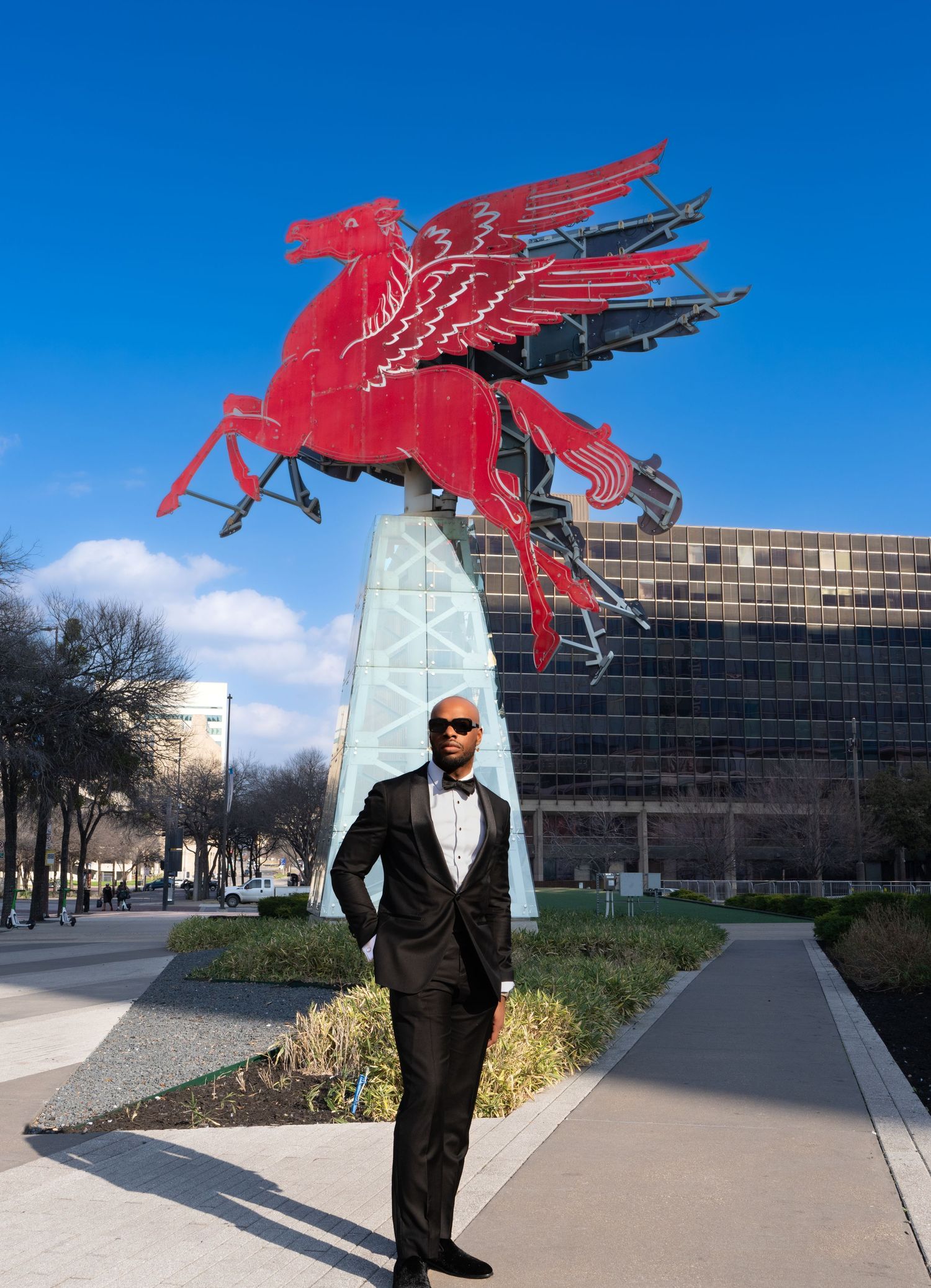 Large red Pegasus sculpture mounted on white pedestal against blue sky and modern building.