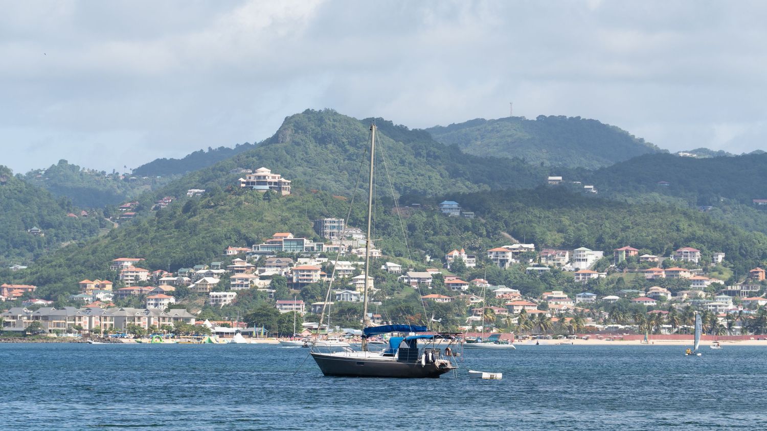 Panoramic view of a tropical coastline with mountains, buildings, and boats in the harbor.