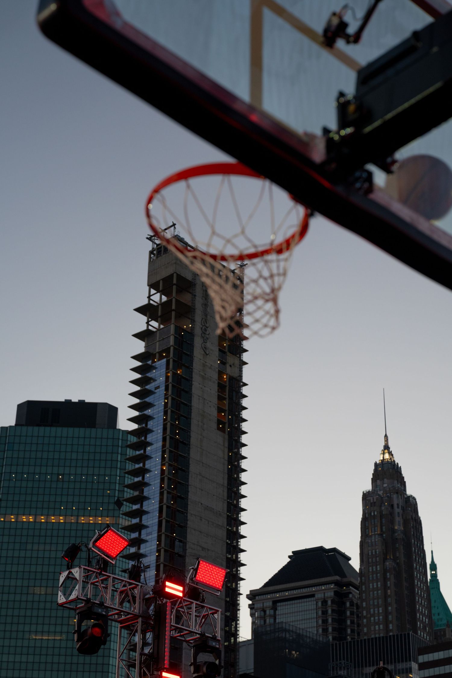 Basketball hoops and urban skyline silhouetted against evening sky.