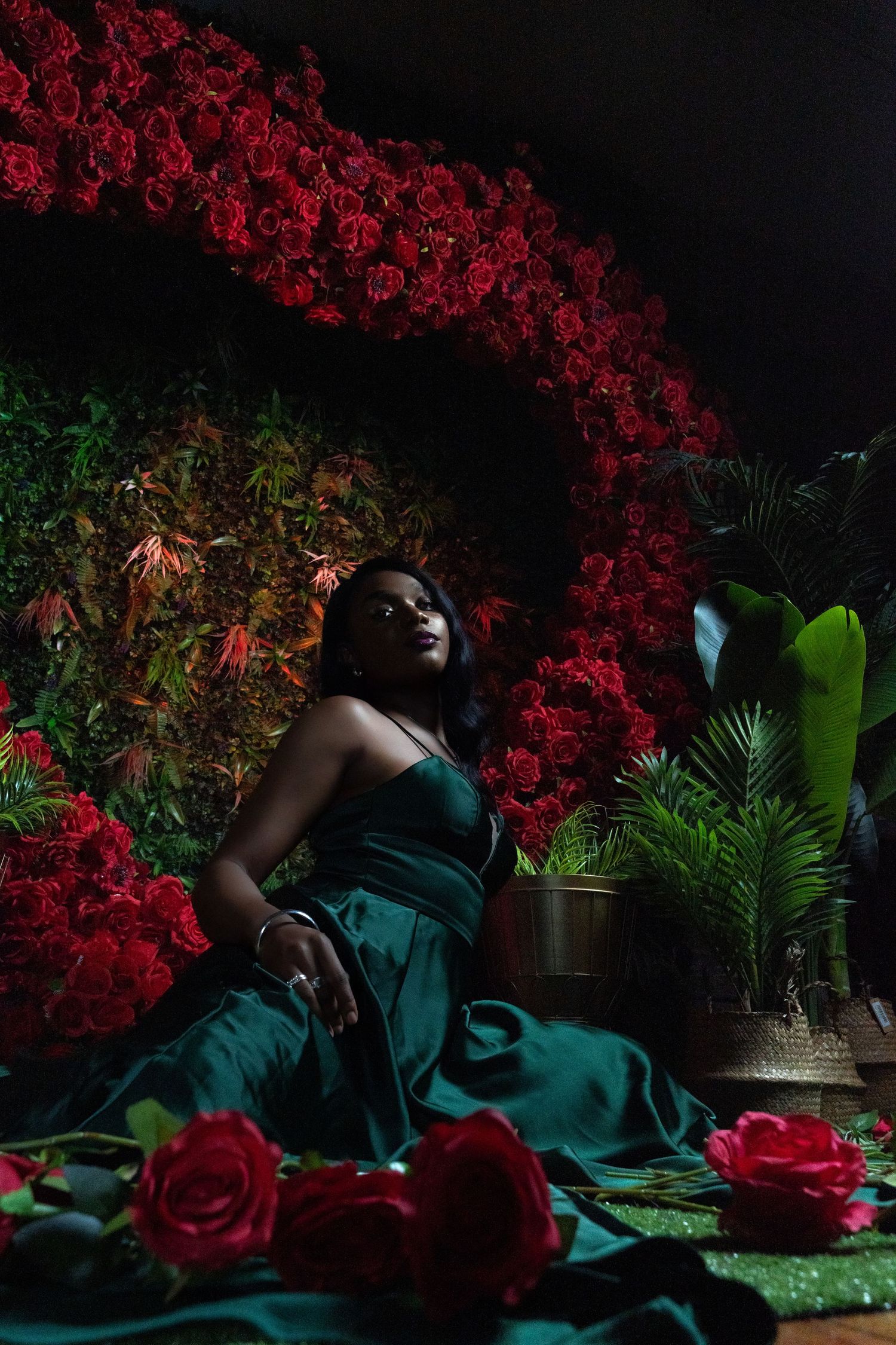 Dramatic portrait scene with red roses and green foliage in dark lighting.