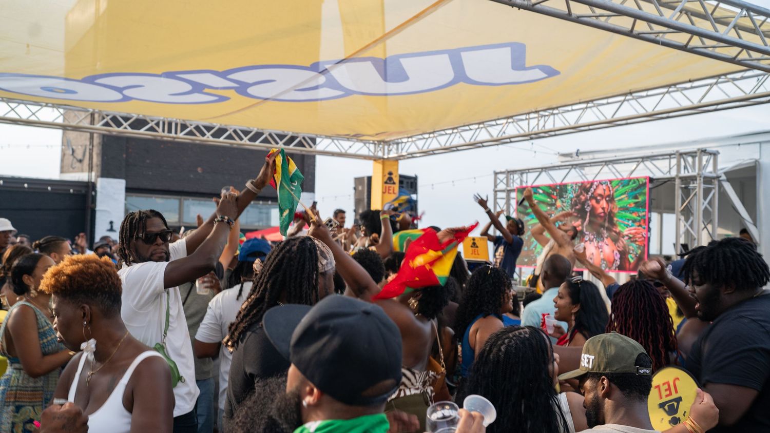 Energetic crowd dancing and celebrating at an outdoor music festival under a tent structure.