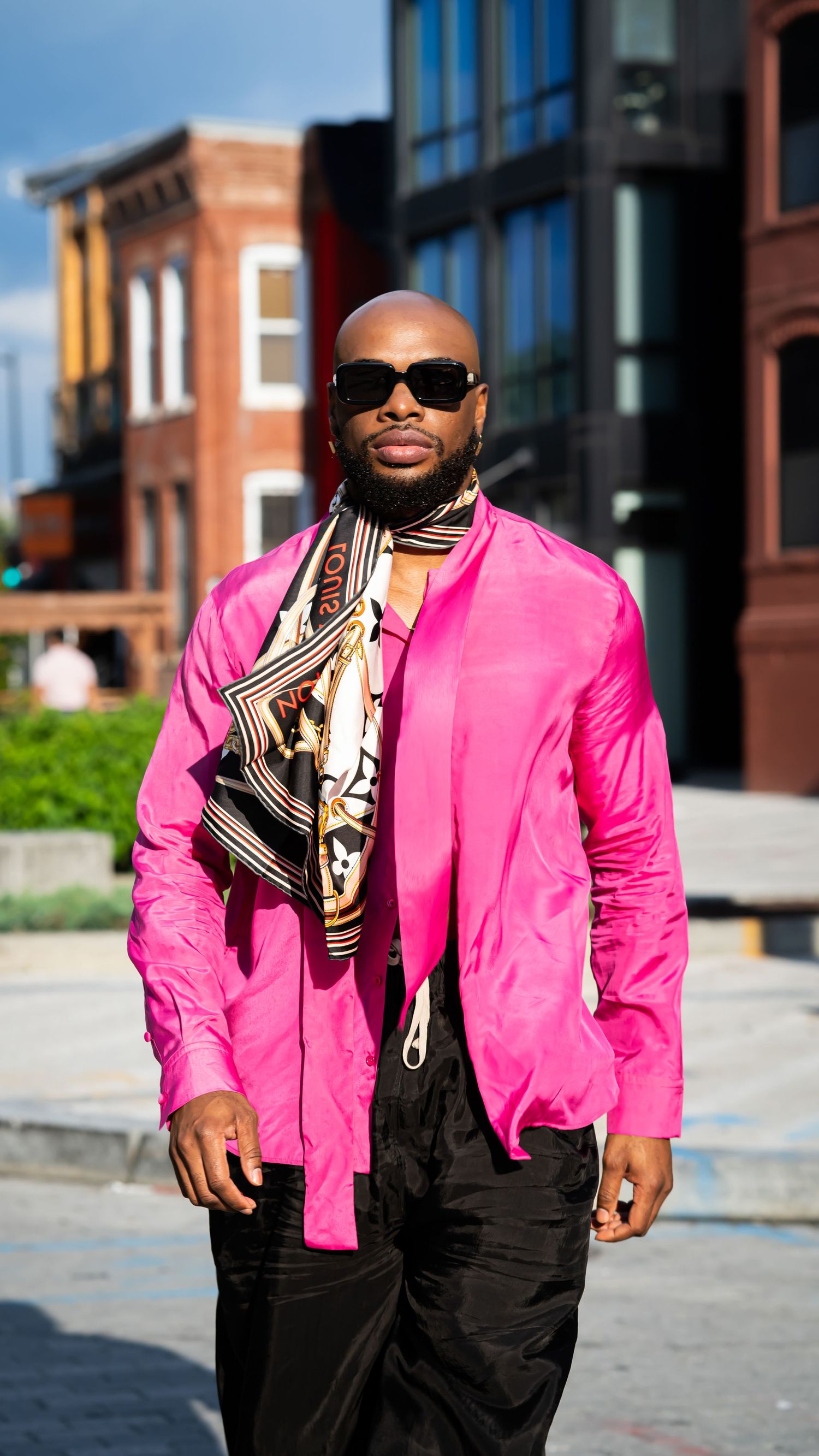 Person wearing bright pink blazer and patterned scarf in urban setting.