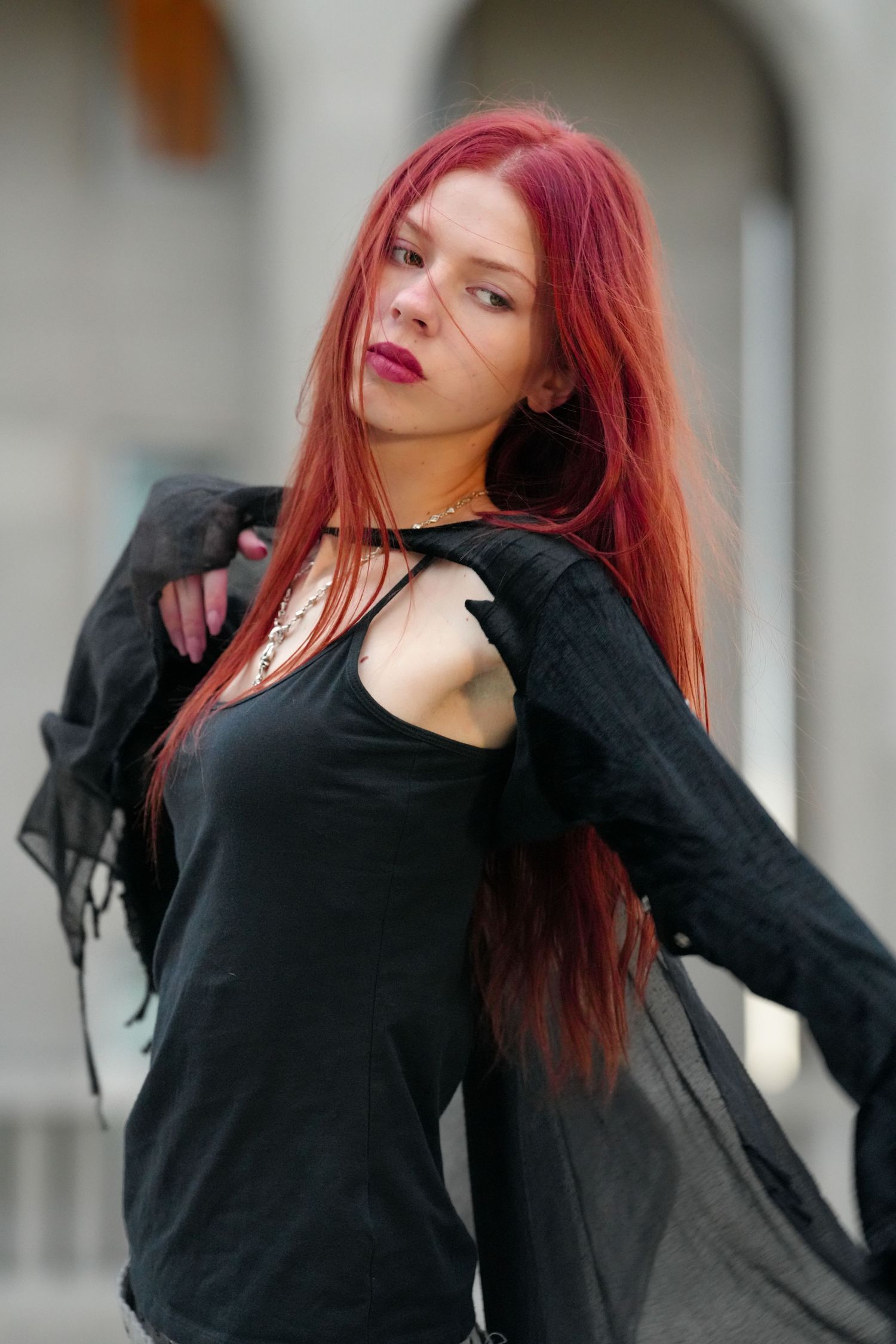 Woman with vibrant red hair dancing in flowing black outfit against light background.