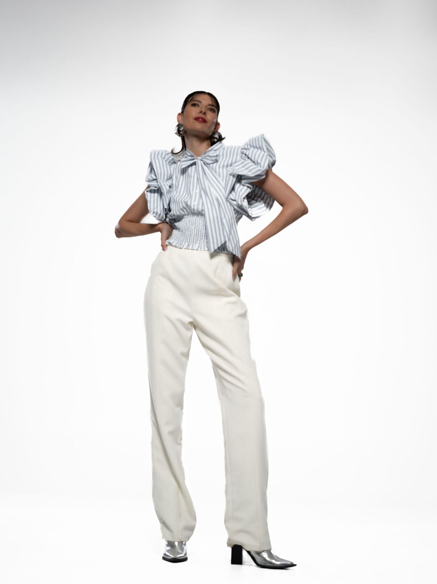 Model strikes dynamic poses wearing striped blouse and white pants against white backdrop.