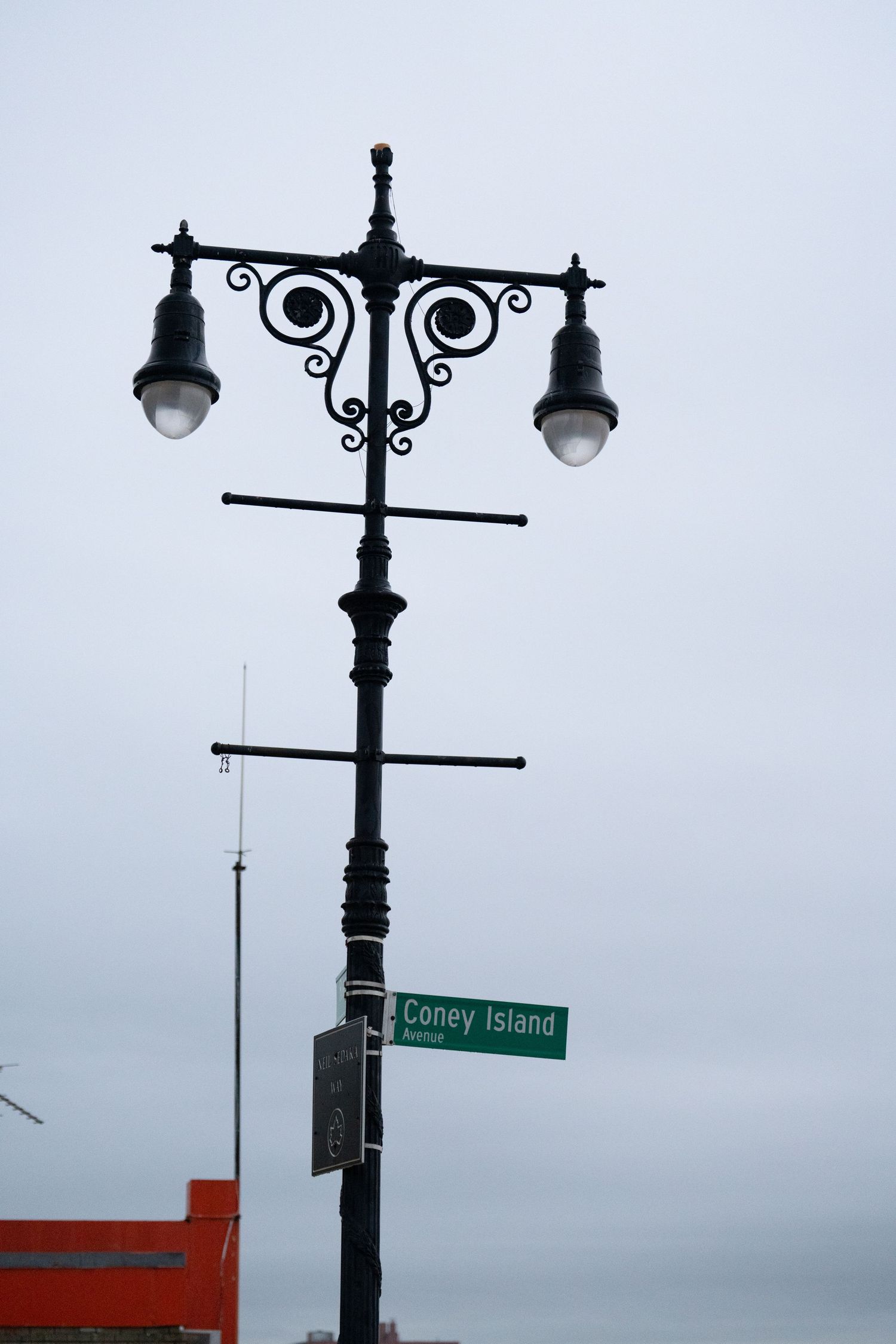 Ornate vintage street lamps and Coney Island street sign against overcast sky.