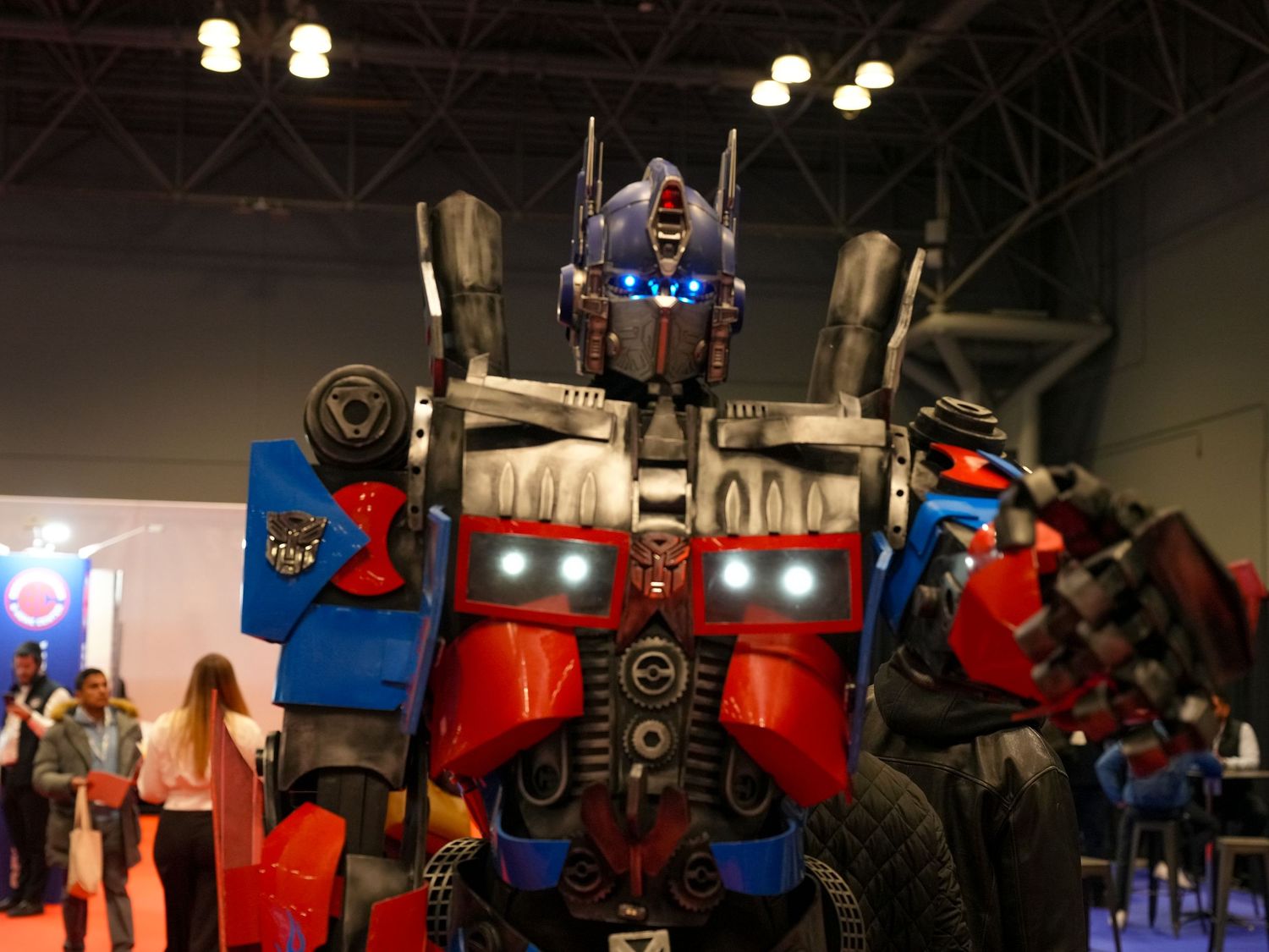 Life-size Optimus Prime Transformers costume display at an indoor convention event with blue glowing eyes.