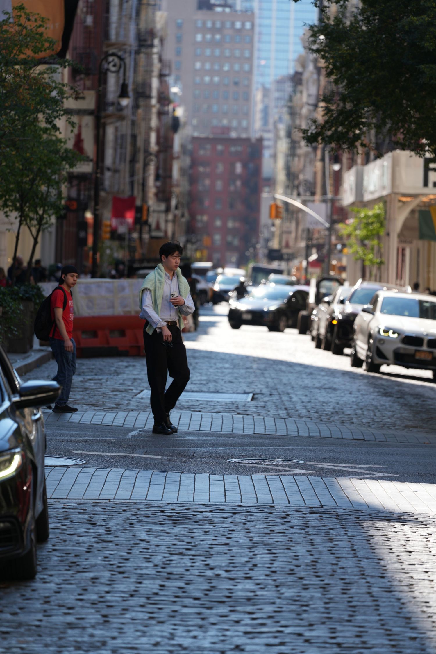 Cobblestone street in New York City with parked cars and tall buildings creating an urban canyon.