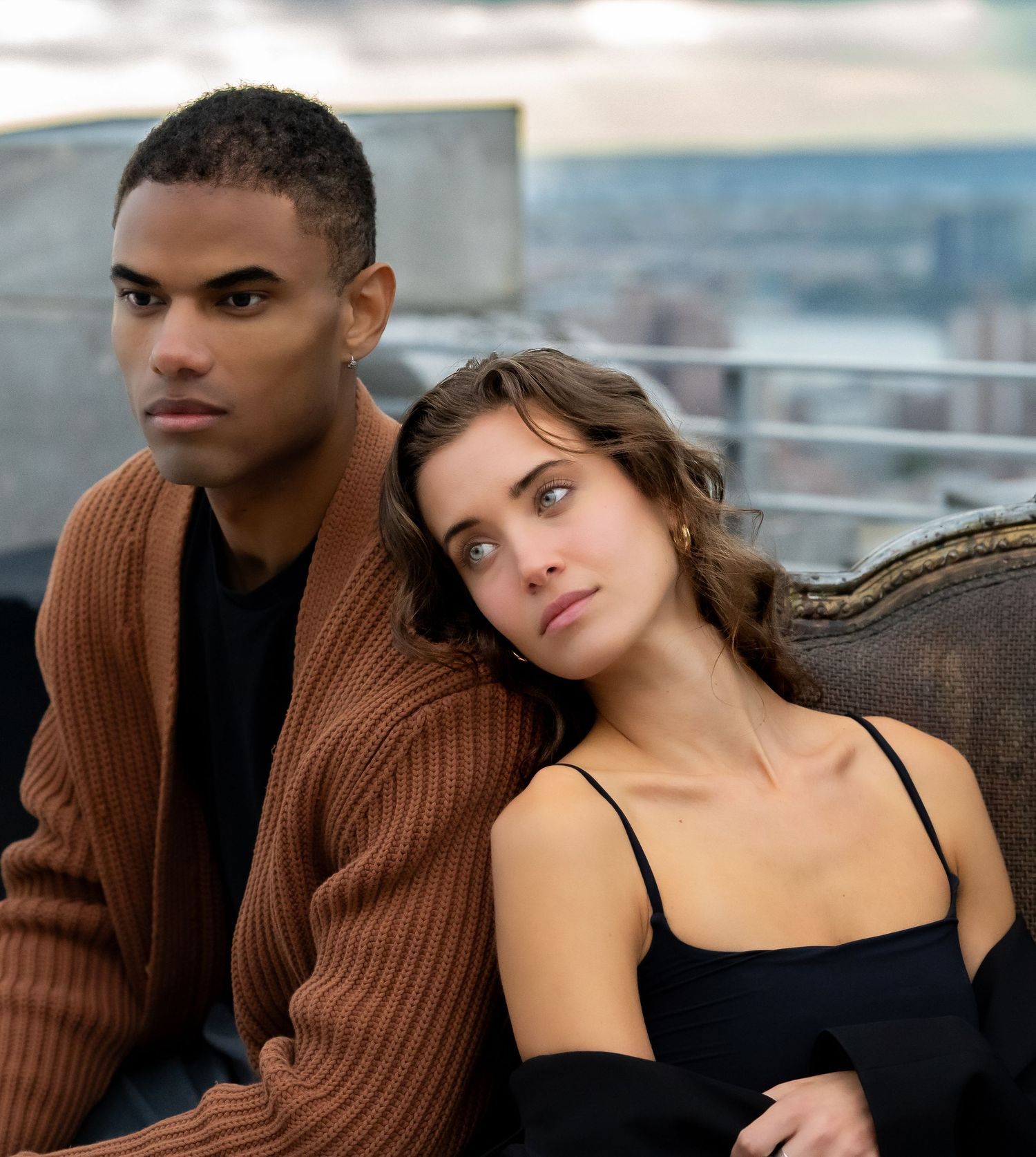 Intimate couple portrait with brown sweater and black top against city skyline.