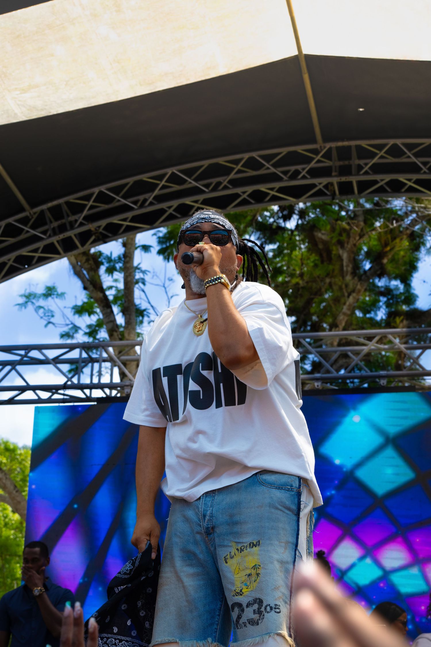 Performer in white WSHN t-shirt and jeans on stage at an outdoor music festival.