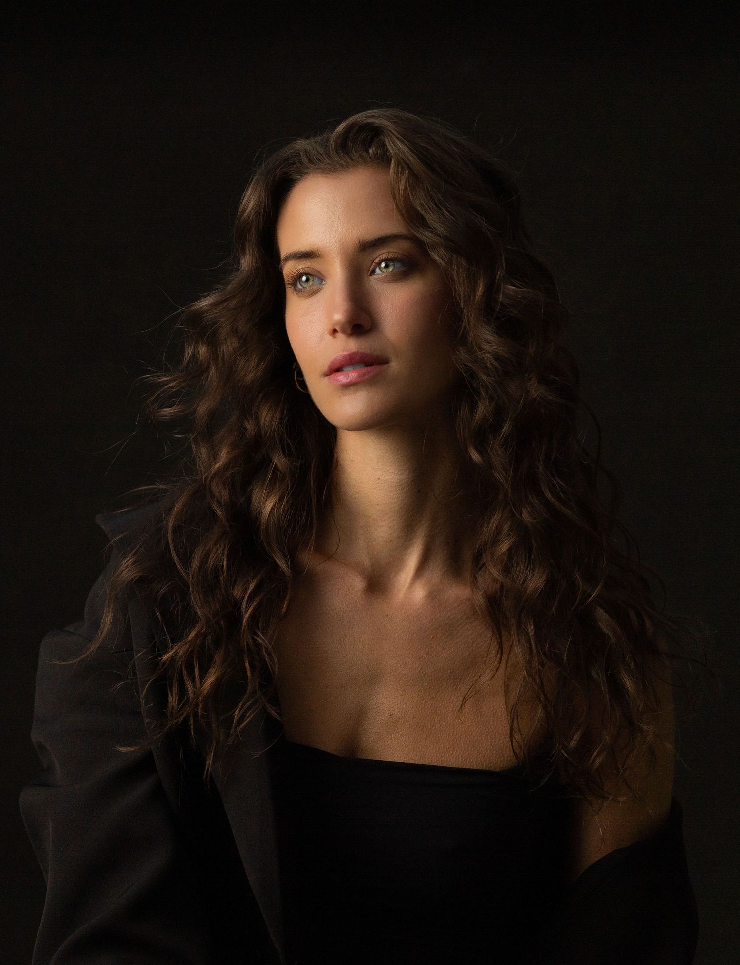 Dramatic portrait against dark background with moody lighting and flowing hair.