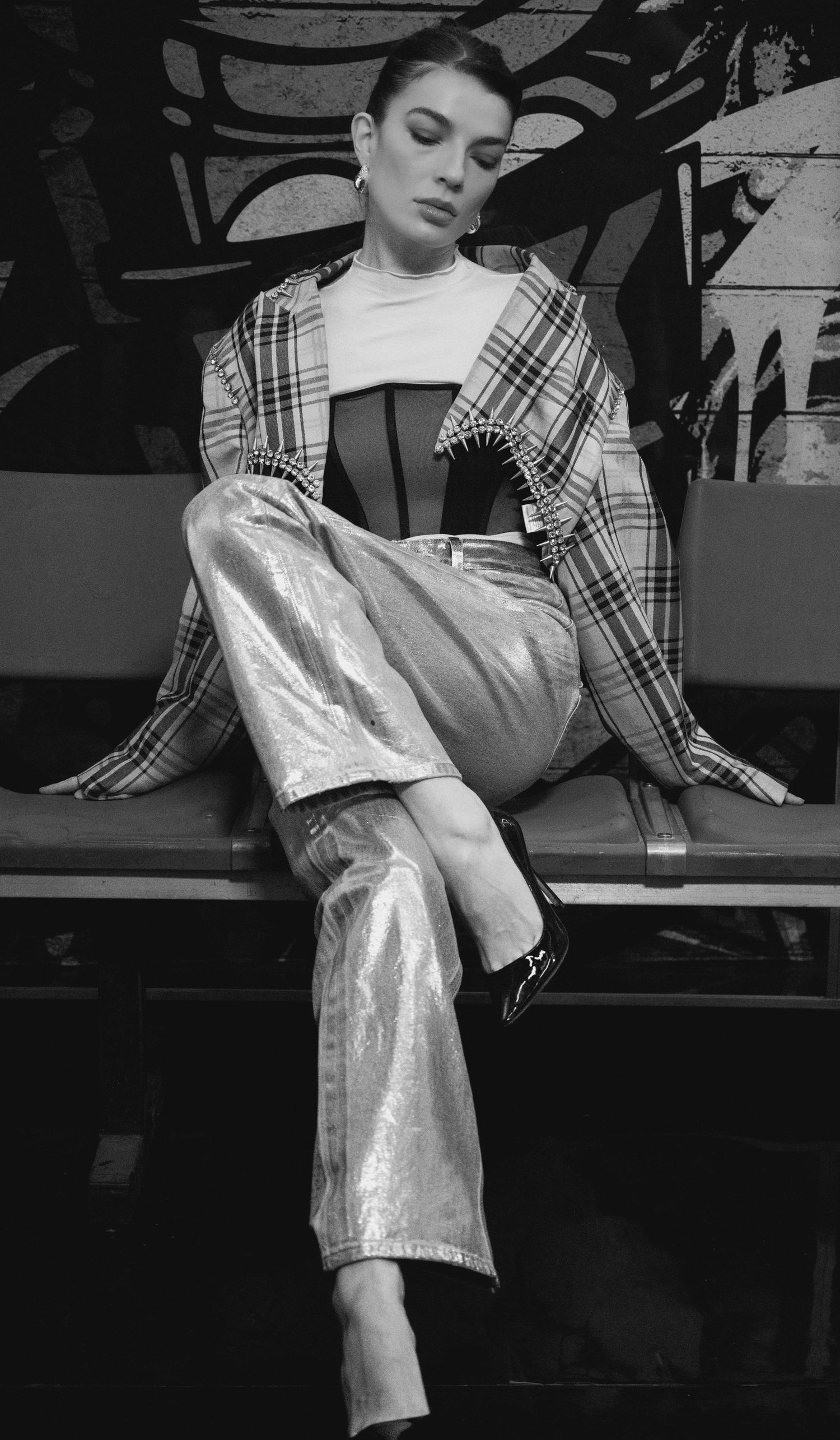 Model in plaid and metallic silver outfit posing artistically in black and white photo.
