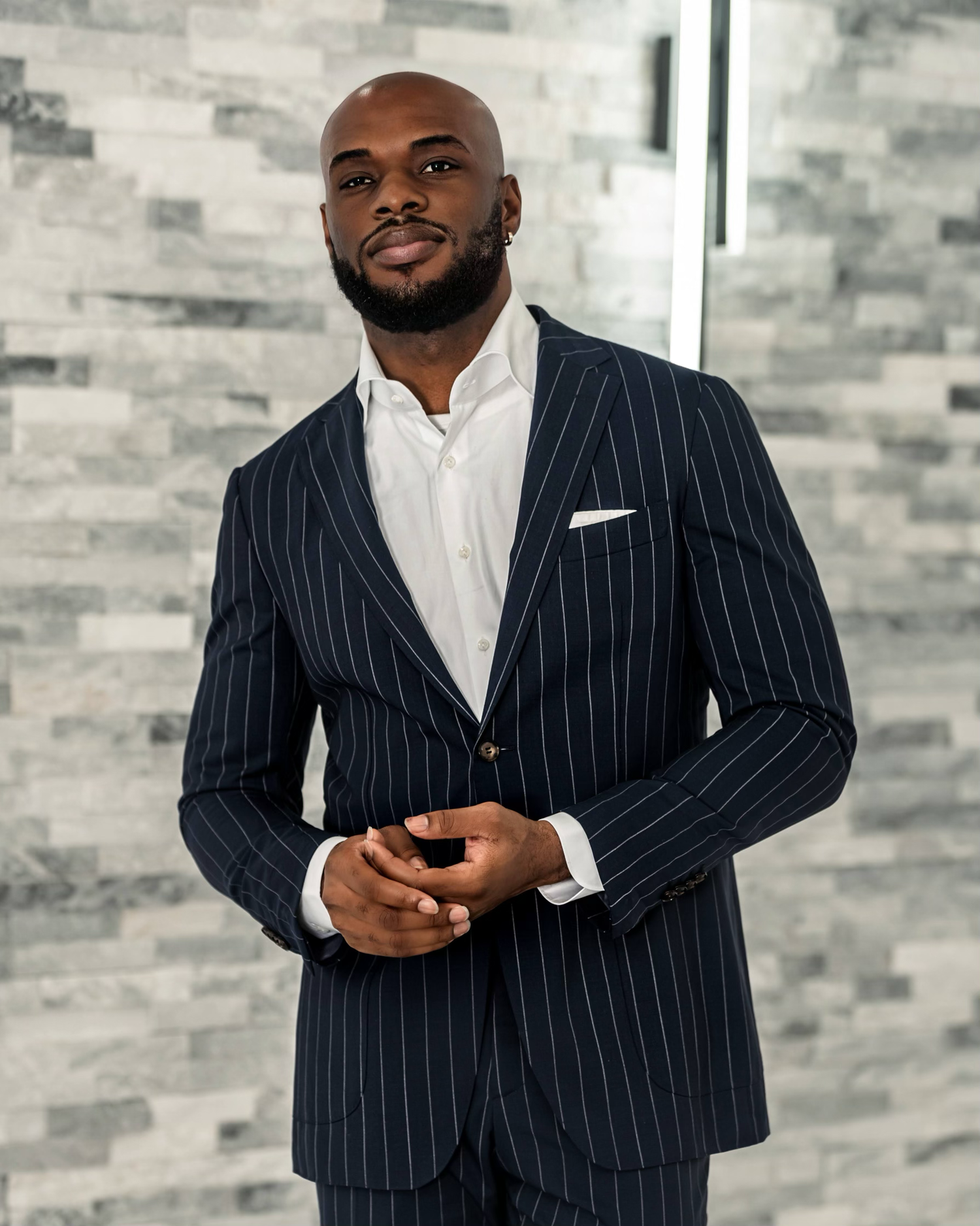 Professional wearing a navy pinstripe suit with white dress shirt in modern office setting.
