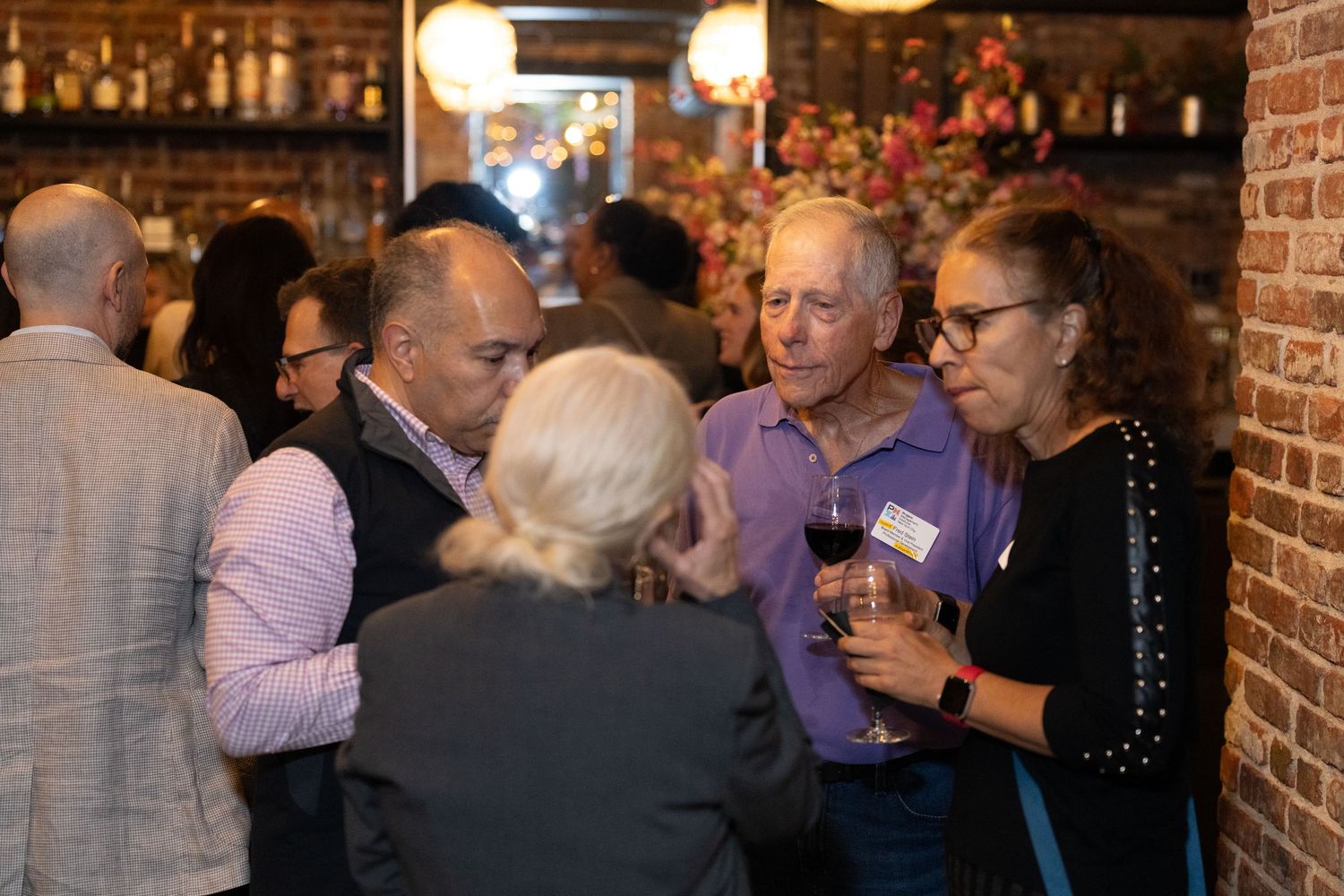People mingling at an indoor social gathering with brick walls and ambient lighting.
